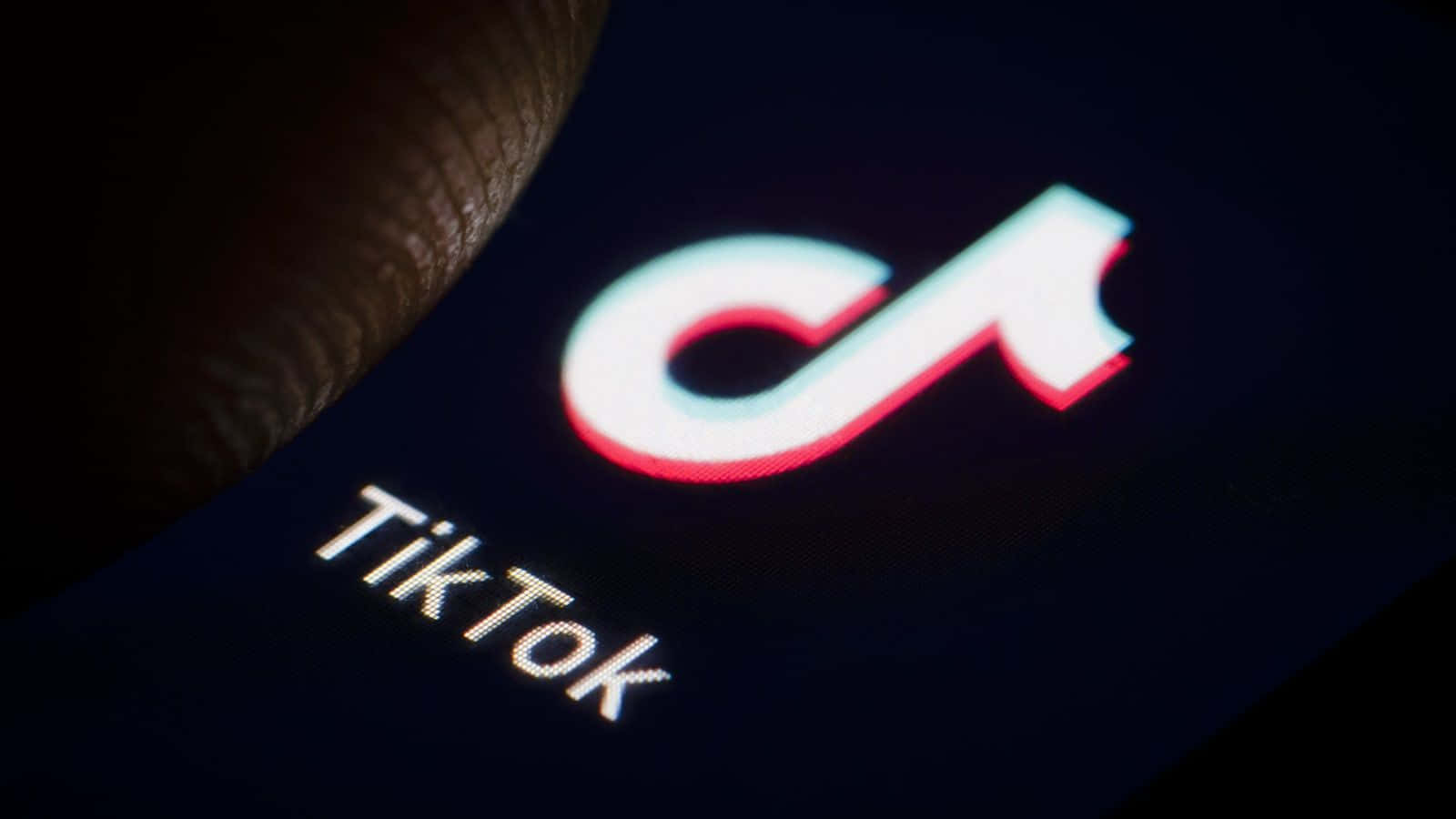 智慧型手機 桌布 壁紙 — 手指觸摸黑暗智慧型手機螢幕上發光的TikTok標誌的特寫。