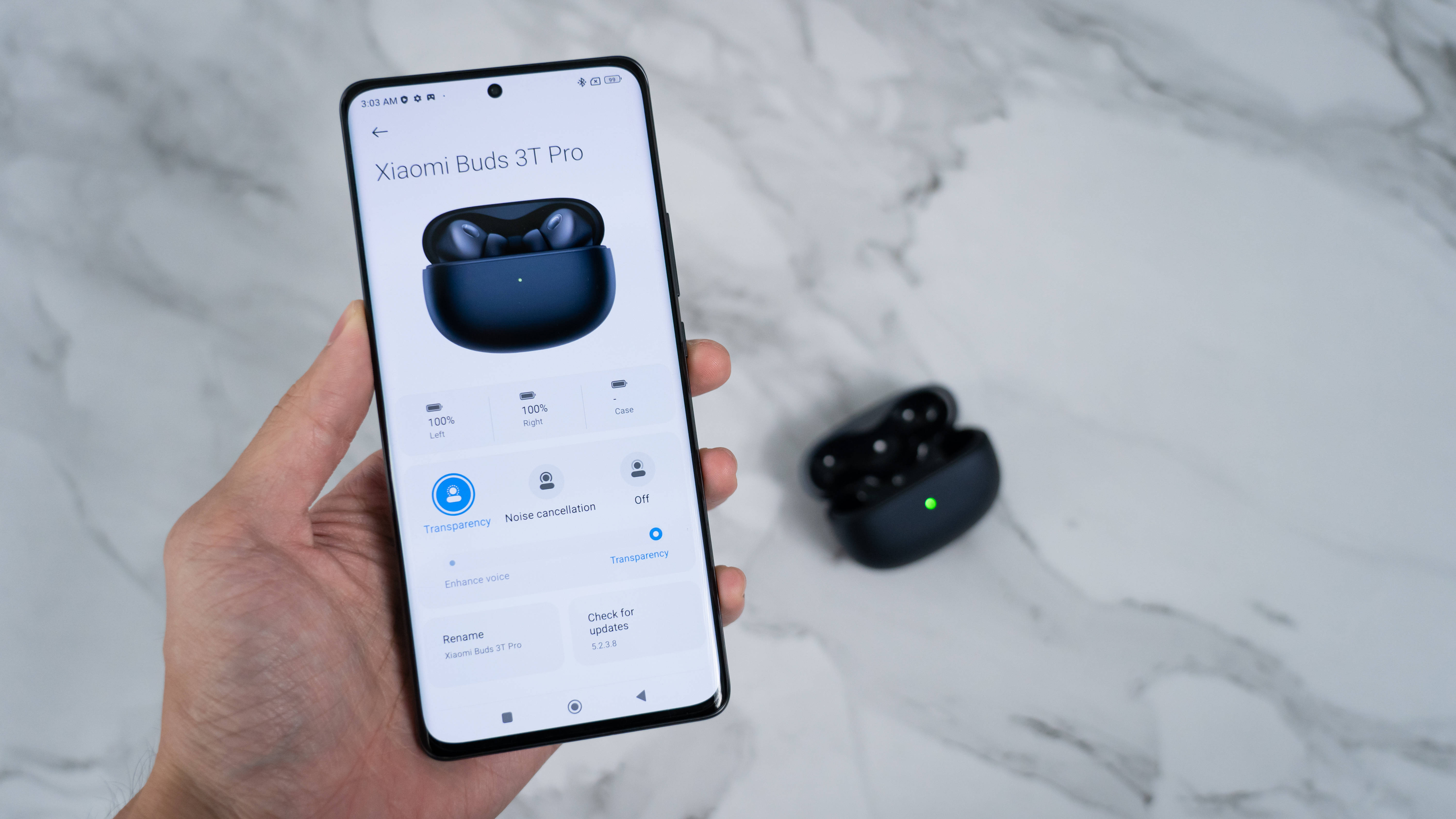Xiaomi 桌布 壁紙 — 手握住智慧型手機，顯示Xiaomi Buds 3T Pro設定，而實際耳機則放在附近的大理石表面上。