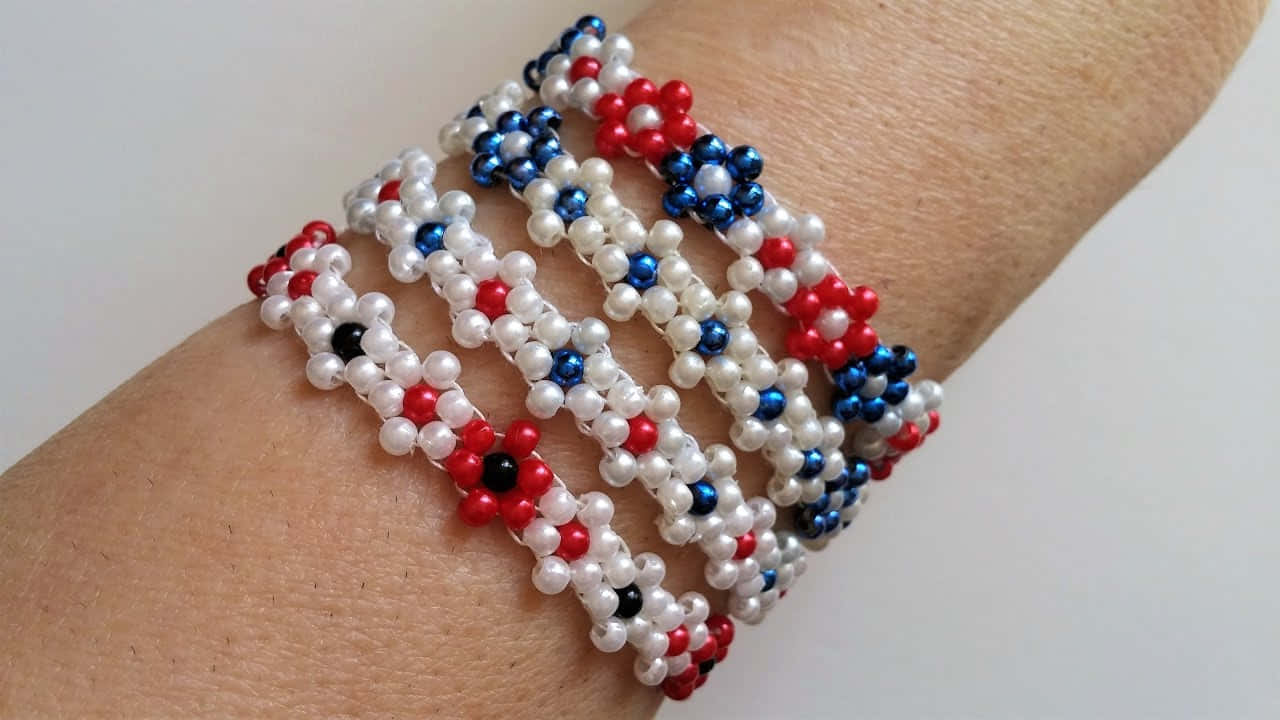 Bead 桌布 壁紙 — 手腕上戴著一條多股串珠手鍊，上面有由珍珠和種子珠製成的紅、藍、白色花卉圖案。