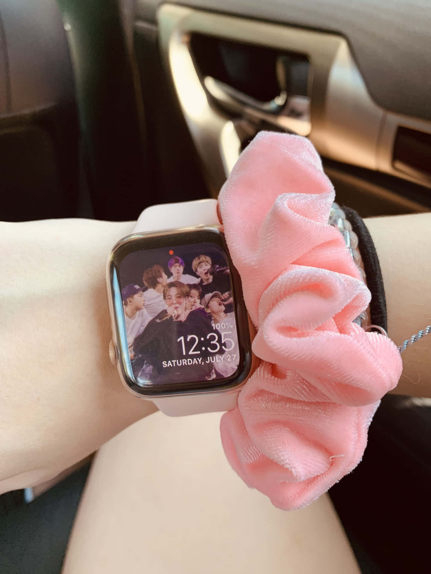 手腕戴粉紅色髮圈和智慧手錶，顯示車內K-pop團體照片。 — Apple Watch 動態 壁紙