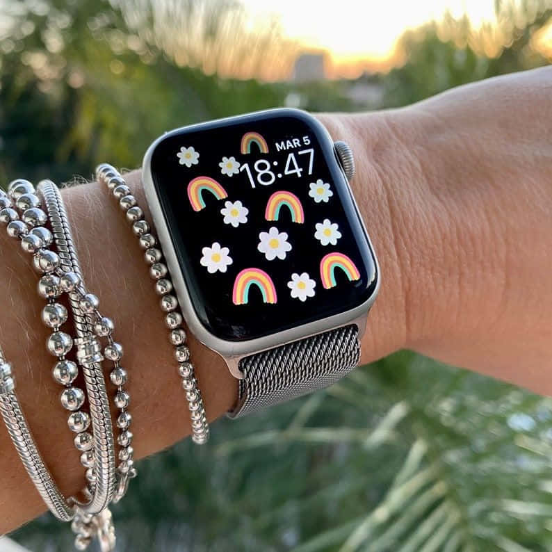 手腕戴銀手鐲和智慧手錶，顯示日落彩虹雛菊桌布。 — Apple Watch 動態 壁紙