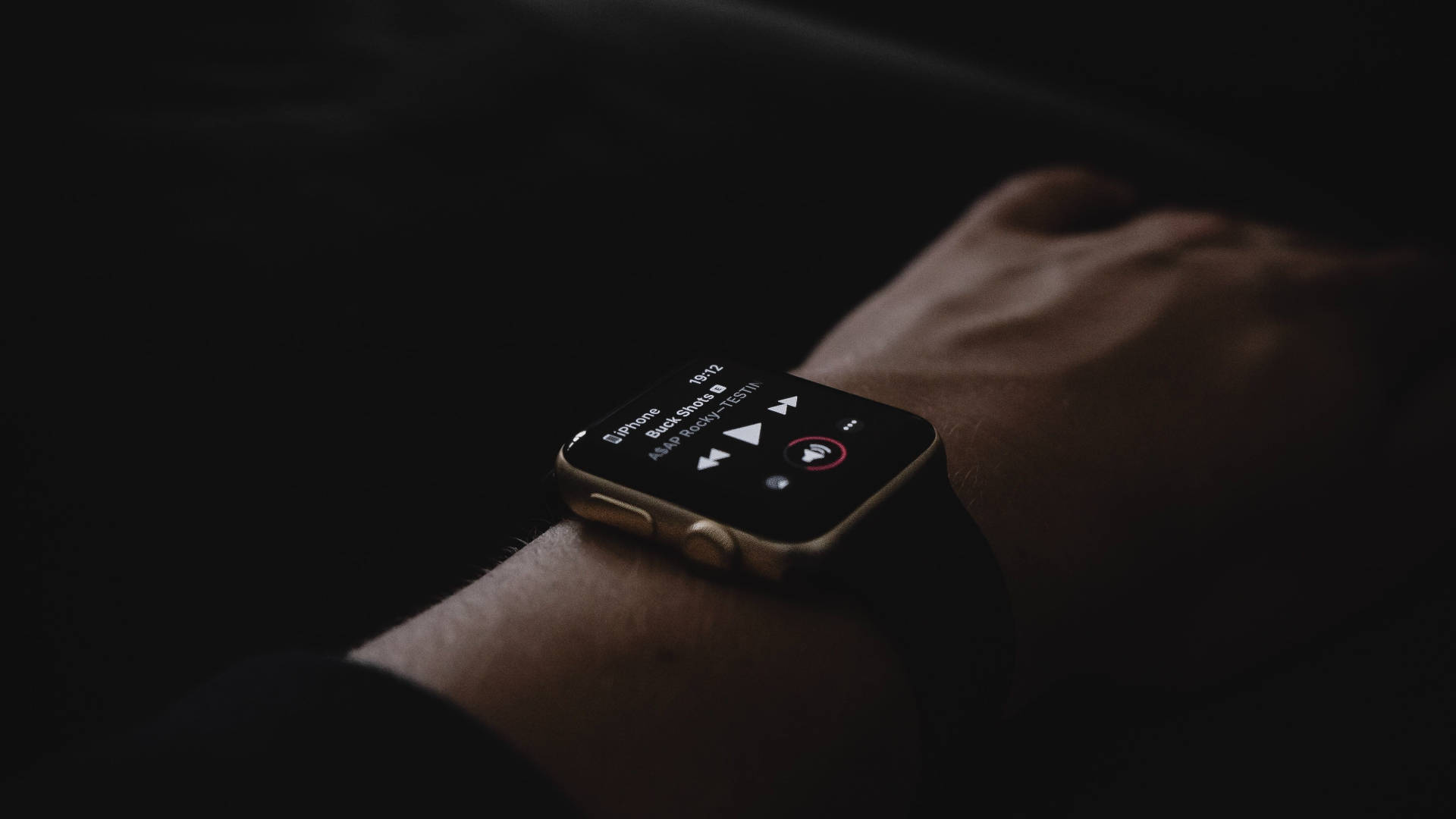 Apple Watch 動態 桌布 壁紙 — 手腕上智慧手錶在昏暗燈光及深色背景下播放音樂的特寫。