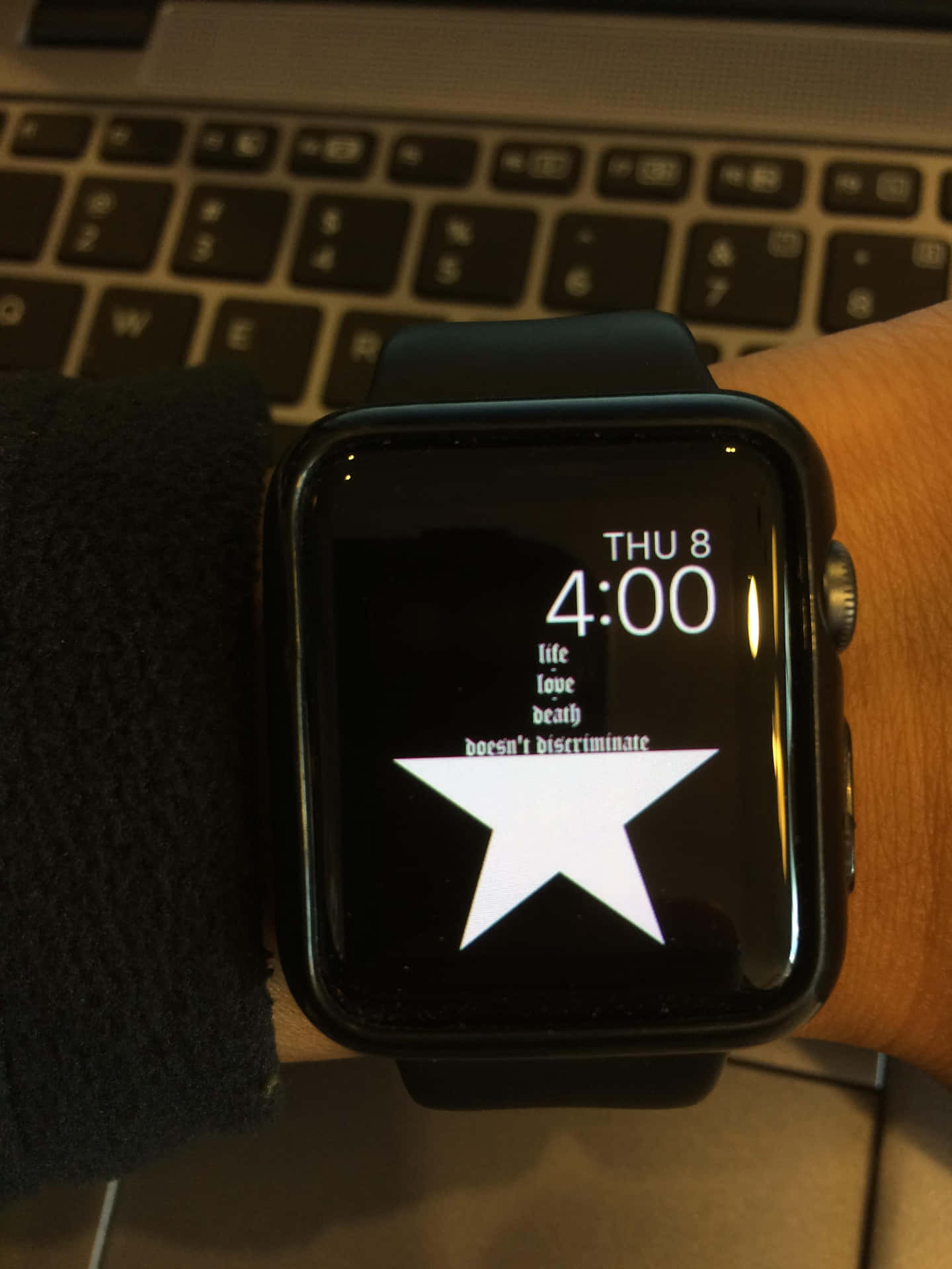 Apple Watch 動態 桌布 壁紙 — 手腕上黑色智慧手錶的特寫，在黑暗螢幕上顯示白色星星和文字，背景有筆記型電腦鍵盤。