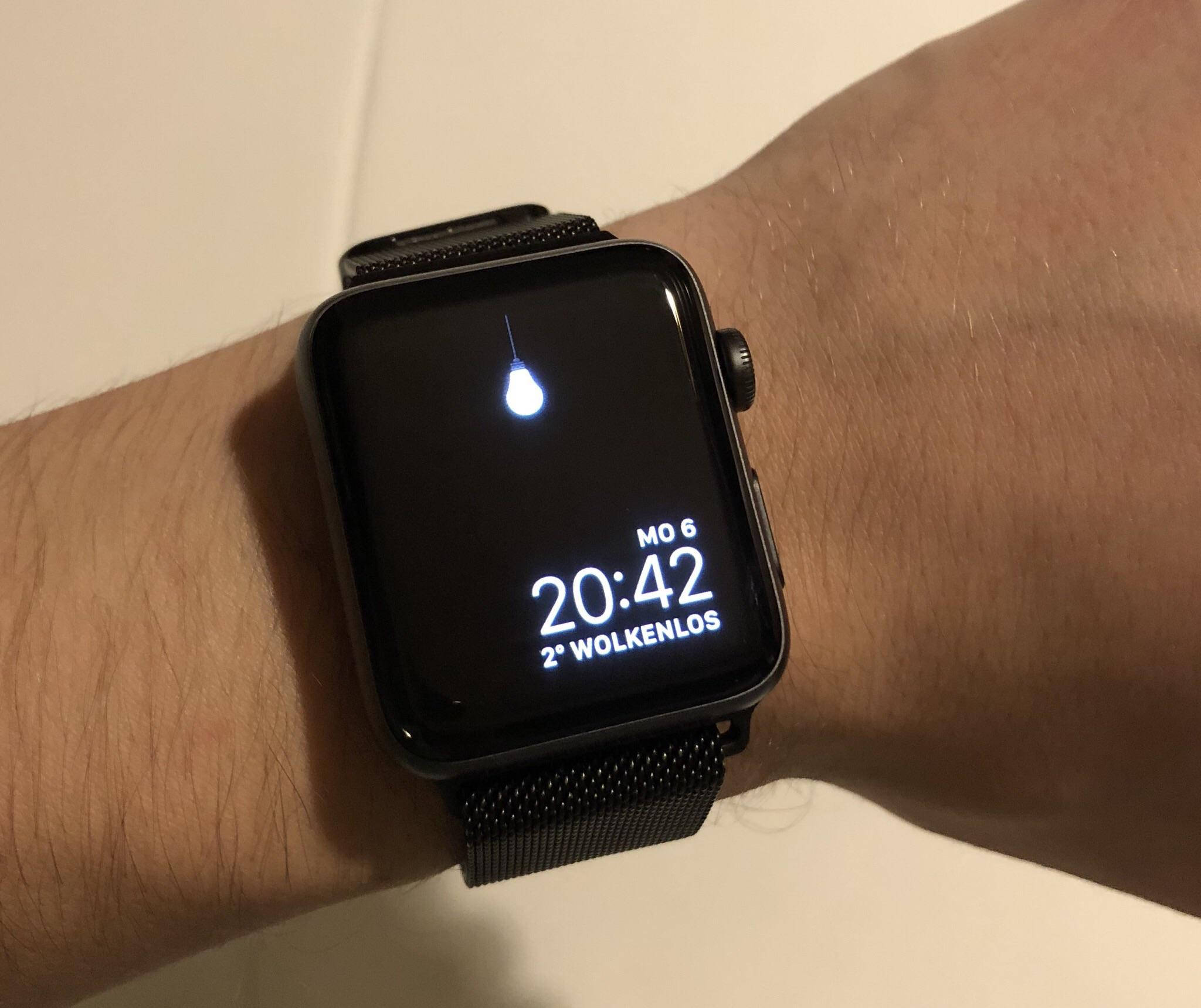 Apple Watch 動態 桌布 壁紙 — 手腕上黑色智慧手錶的特寫，顯示時間、天氣和一個水滴圖示，背景為純色牆壁。
