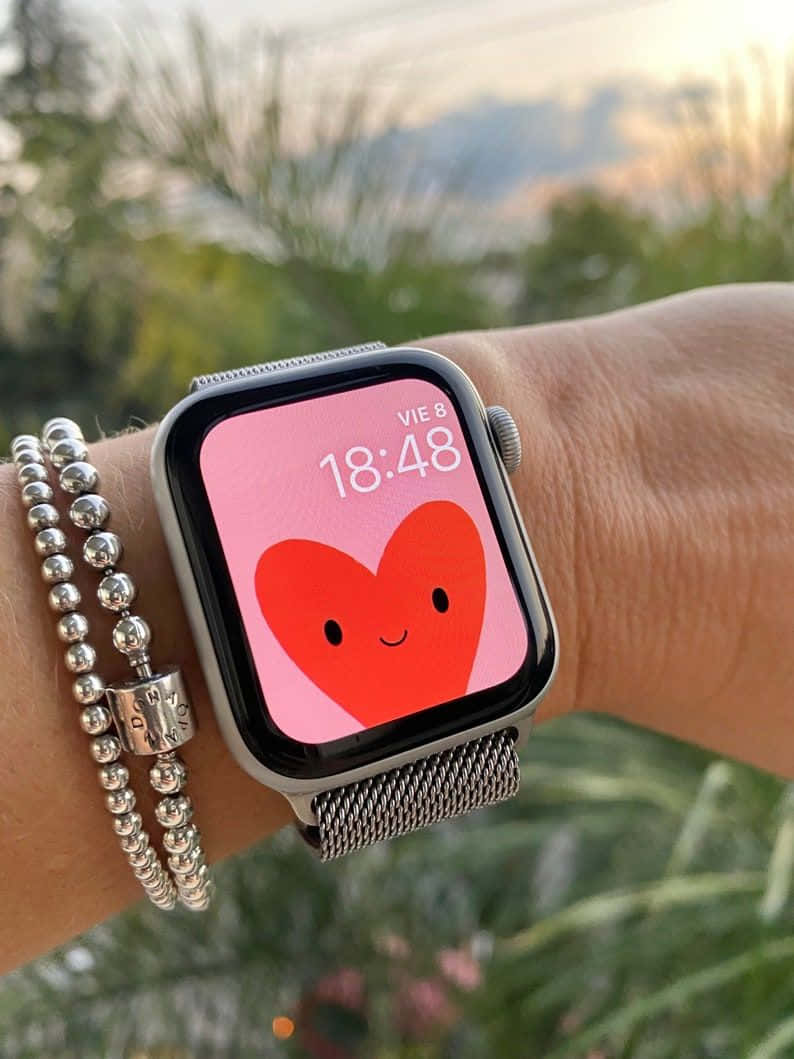 手腕上的智慧手錶在花園日落時顯示心形臉和銀色手鐲。 — Apple Watch 動態 壁紙