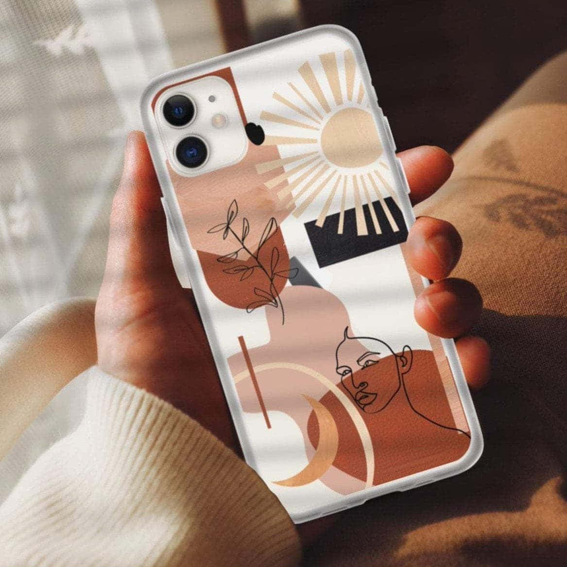 Phone Case 桌布 壁紙 — 手裡拿著手機，手機上有抽象赤陶太陽葉子和臉部設計，背景是柔和窗光。