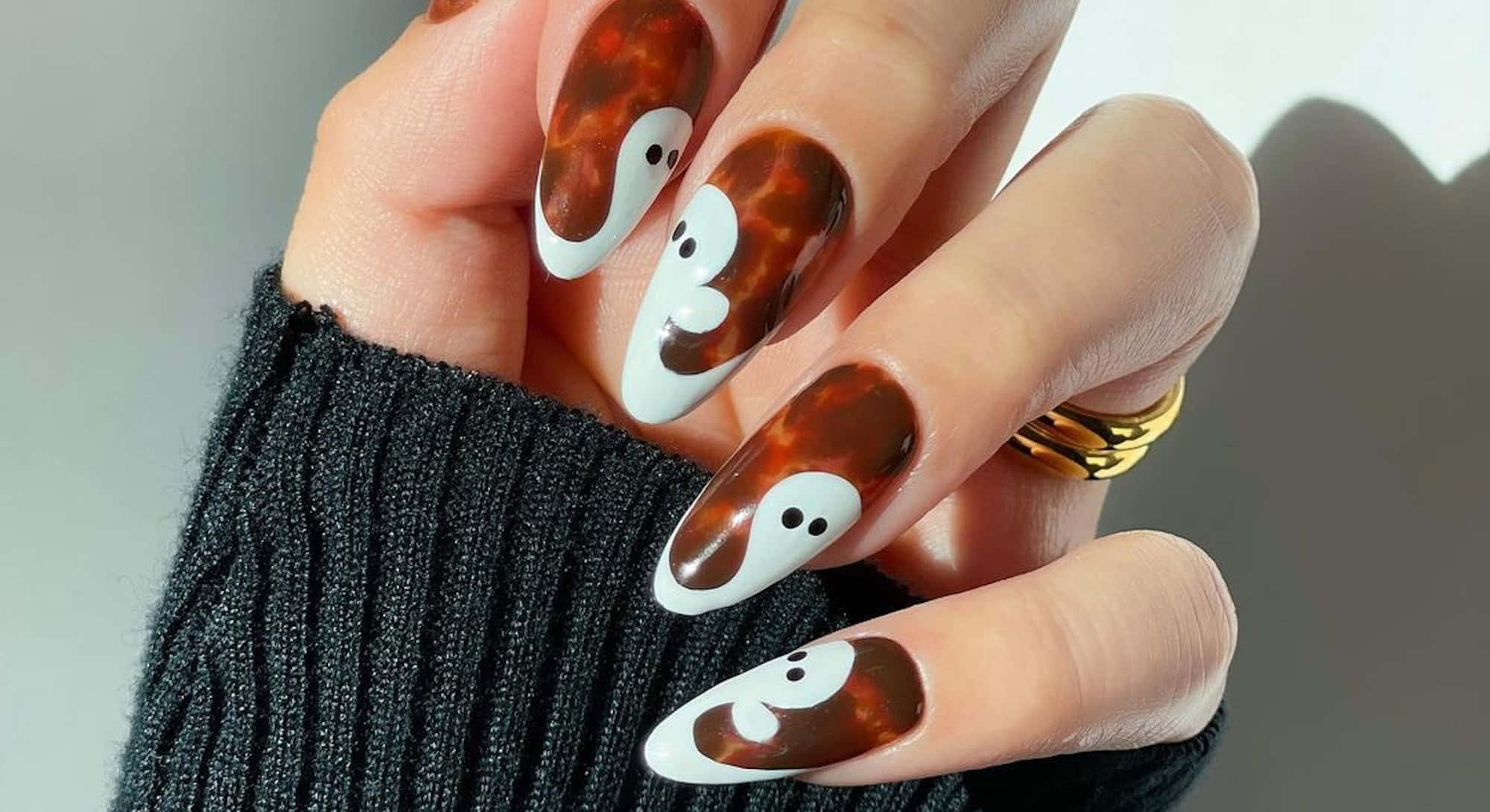 Halloween Nail Art 桌布 壁紙 — 手部帶有光澤的玳瑁指甲，配上可愛的白色鬼魂設計，背景為柔和灰色。