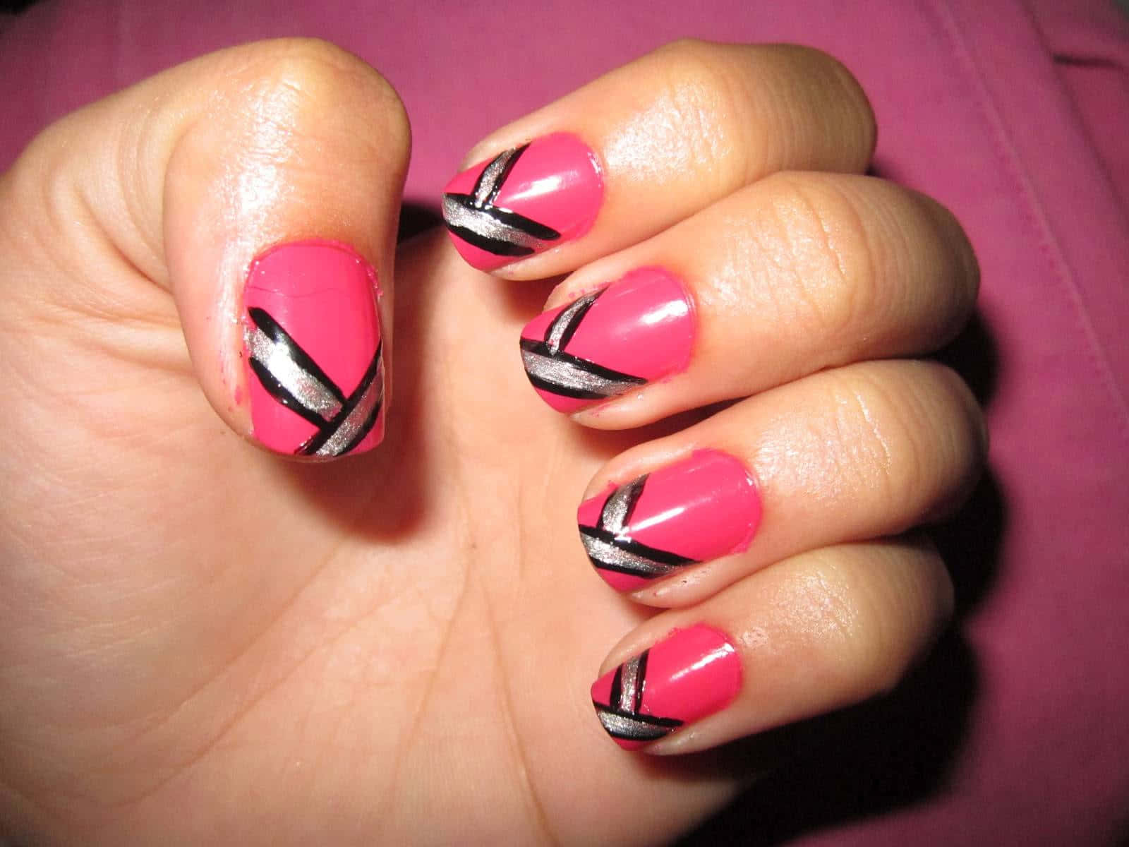Cute Nails 桌布 壁紙 — 手部特寫，亮粉紅色指甲帶有醒目黑色和銀色幾何交叉設計。