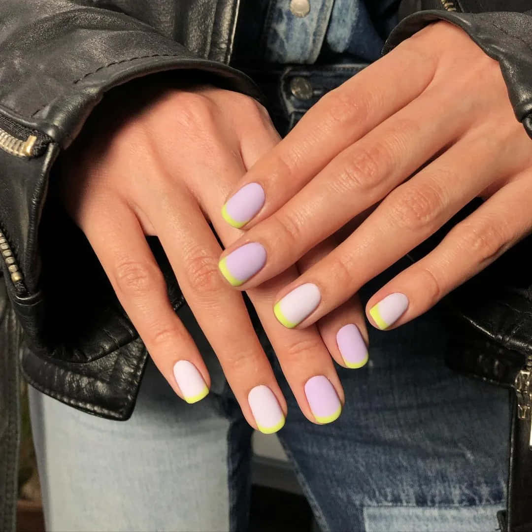 Spring Nails 桌布 壁紙 — 手部特寫，以黑色皮夾克和牛仔布為背景，粉彩薰衣草色和白色指甲配上螢光黃色指尖。