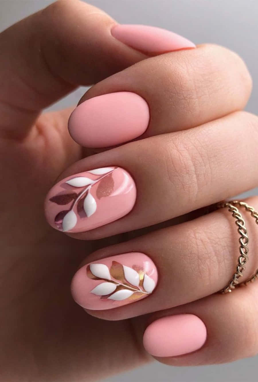Pink Nail Art 桌布 壁紙 — 手部特寫，兩隻手指上有柔和的粉紅色指甲，帶有精緻的白色和金色葉片設計。