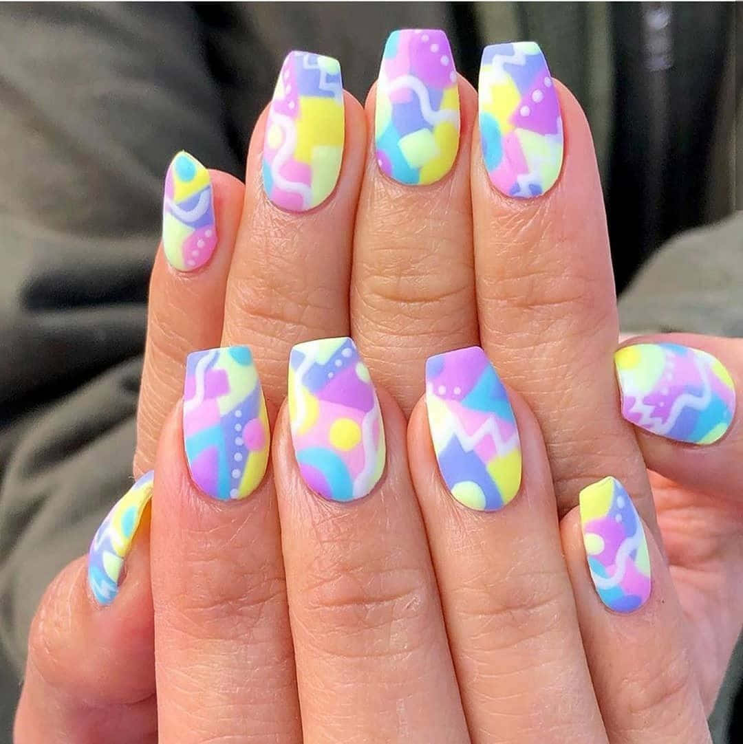 Spring Nails 桌布 壁紙 — 手部特寫，帶有充滿活力的粉彩幾何指甲藝術，包括粉紅色、黃色、藍色和紫色的漩渦、圓點和抽象形狀。
