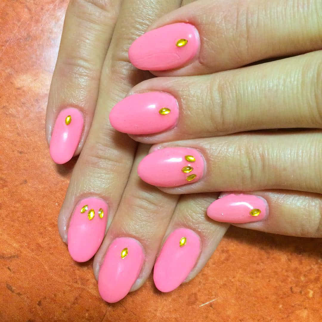 Pink Nails 桌布 壁紙 — 手部特寫，帶有光澤的粉紅色指甲，飾有小金色水鑽，背景為溫暖的陶土色。
