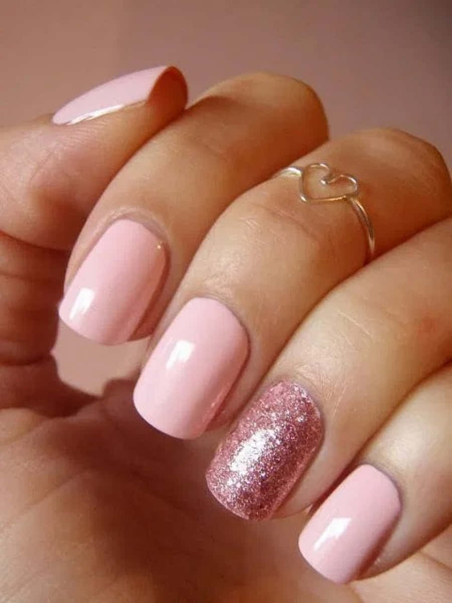 Pink Nail Art 桌布 壁紙 — 手部特寫，帶有柔和粉紅色指甲、一隻閃亮玫瑰金點綴指甲和精緻心形戒指。