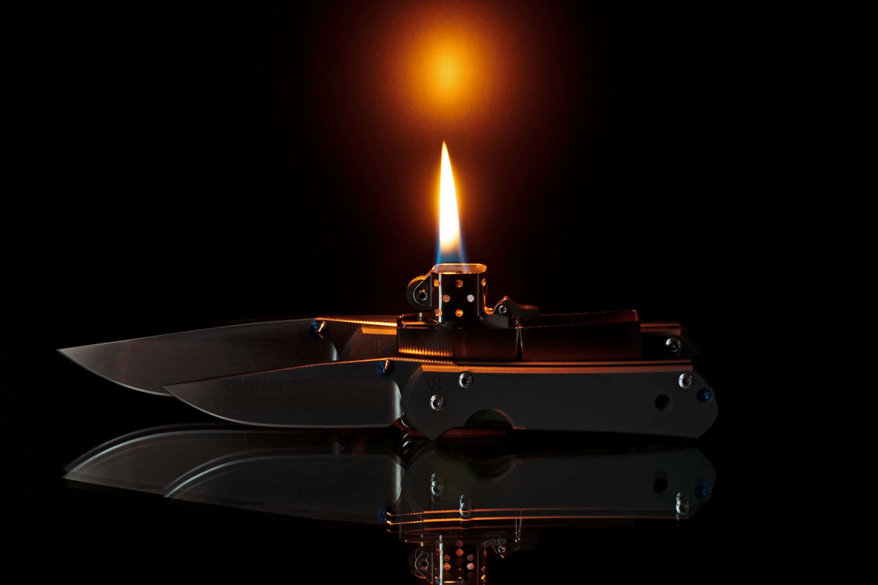 lighter 桌布 壁紙 — 打火機閃爍的火焰在黑色背景的反射表面上為兩把摺刀投下溫暖的光芒。