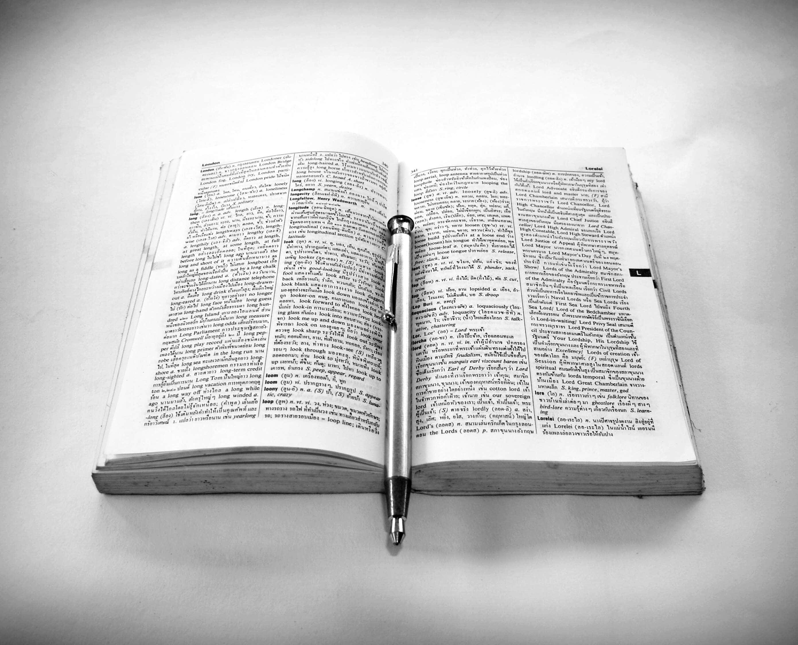 Black And White Book 桌布 壁紙 — 打開字典頁面的特寫，文字密集，頁邊有一幅人物的小型黑白插圖。