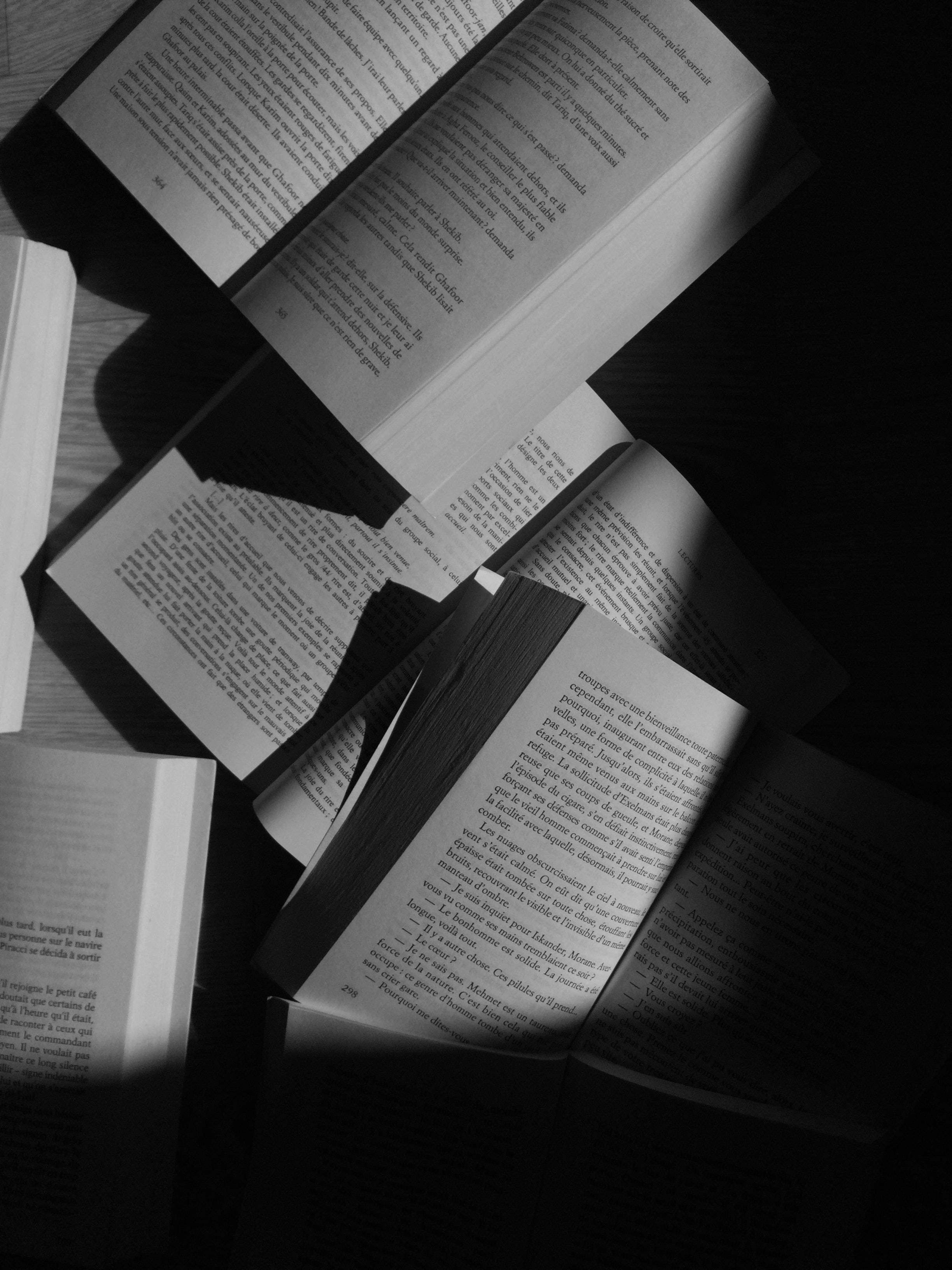 黑白 桌布 壁紙 — 打開的書本散落在木質表面上，沐浴在戲劇性的斜陽光中，投下深深的陰影。
