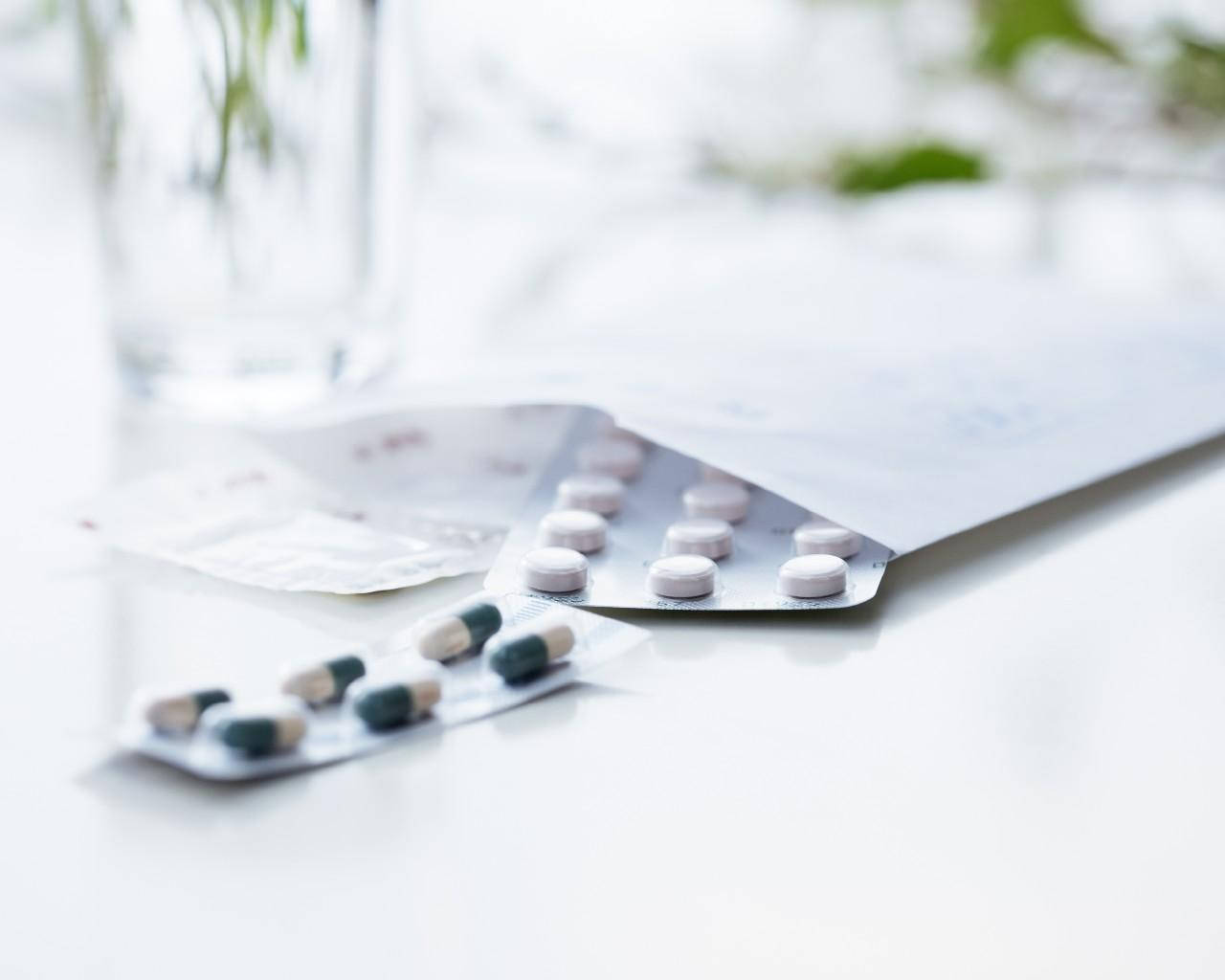 Health 桌布 壁紙 — 打開的藥片泡罩包裝的特寫，藥片放在明亮的白色桌子上，旁邊有一個玻璃杯。