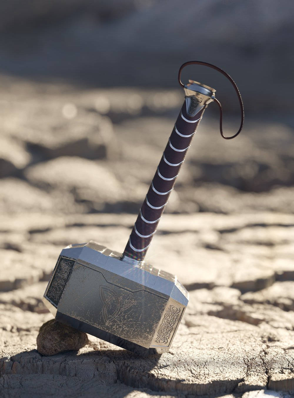 Thors Hammer 桌布 壁紙 — 托爾的錘子妙爾尼爾放在龜裂的地面上，在明亮的陽光下，帶有精細的雕刻和皮革包裹的手柄。