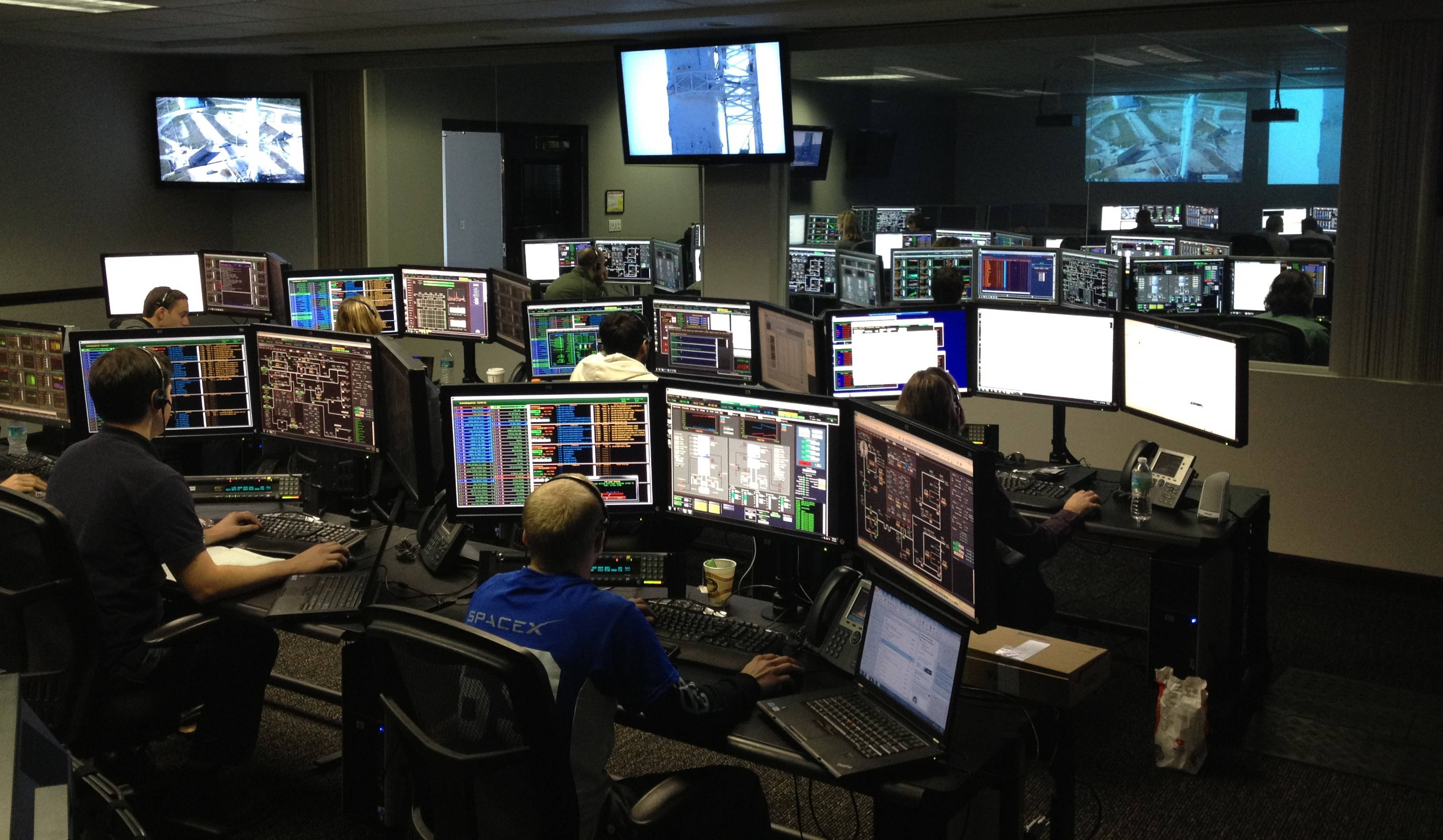Monitor 桌布 壁紙 — 技術人員在光線昏暗的SpaceX控制室中，監控多個顯示複雜數據和即時畫面的螢幕。