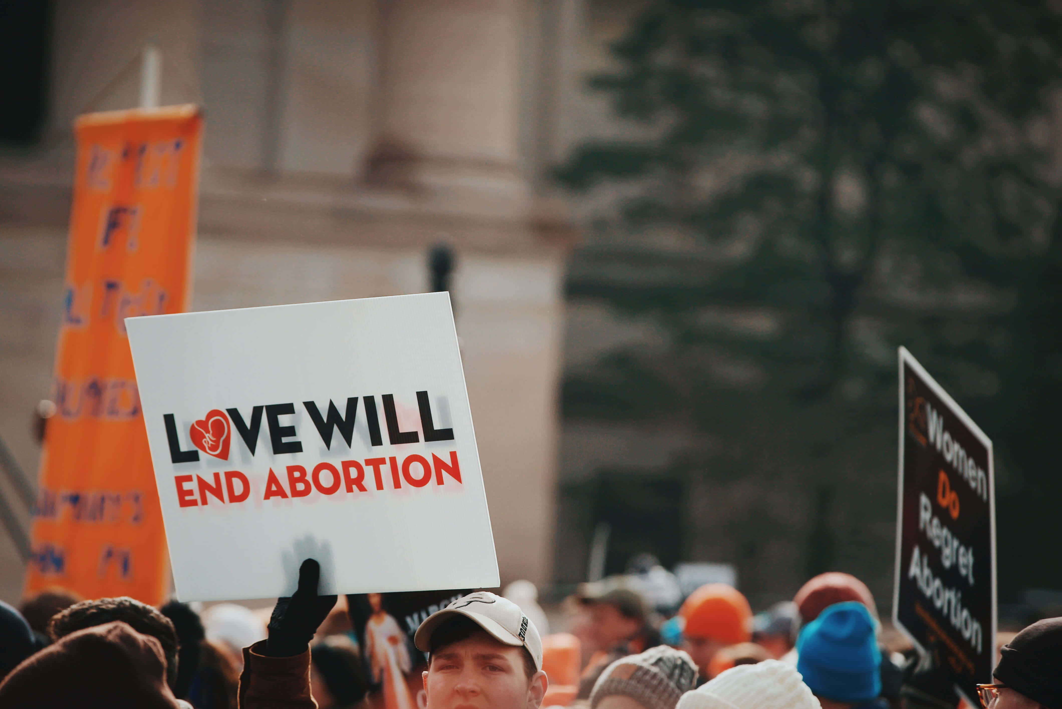 政治 桌布 壁紙 — 抗議者在石建築物前的集會中舉著寫有「LOVE WILL END ABORTION」和「Women Do Regret Abortion」的標語牌。