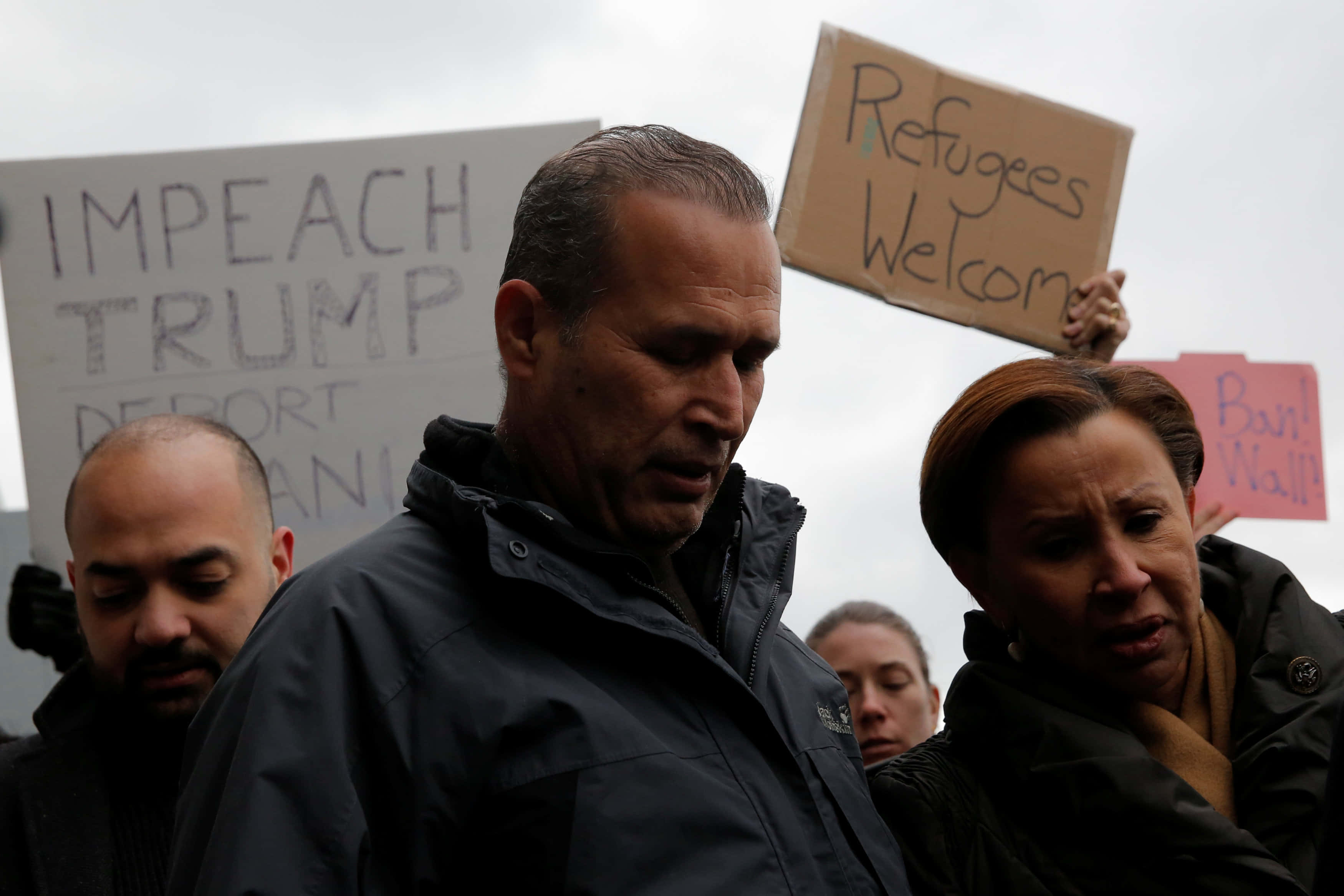 Cloudy Sky 桌布 壁紙 — 抗議者在陰天的天空下舉起寫著「Impeach Trump」和「Refugees Welcome」的手製標語牌。