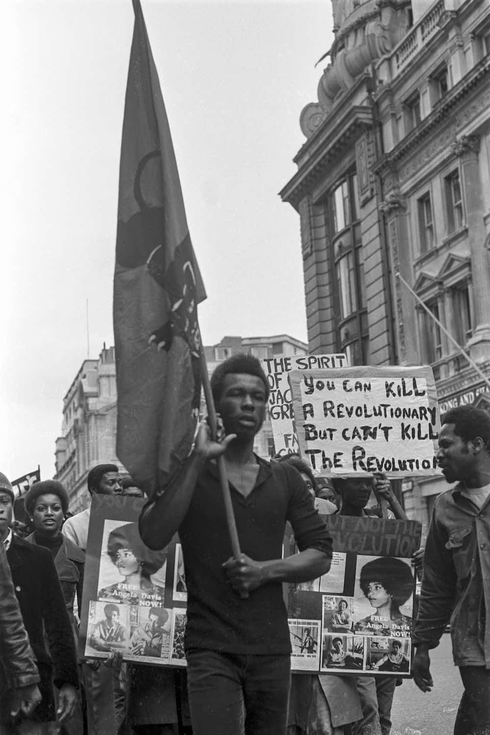 Black Panther Party 桌布 壁紙 — 抗議者手持標語和旗幟，帶著堅定的表情在城市街道上游行的黑白照片。