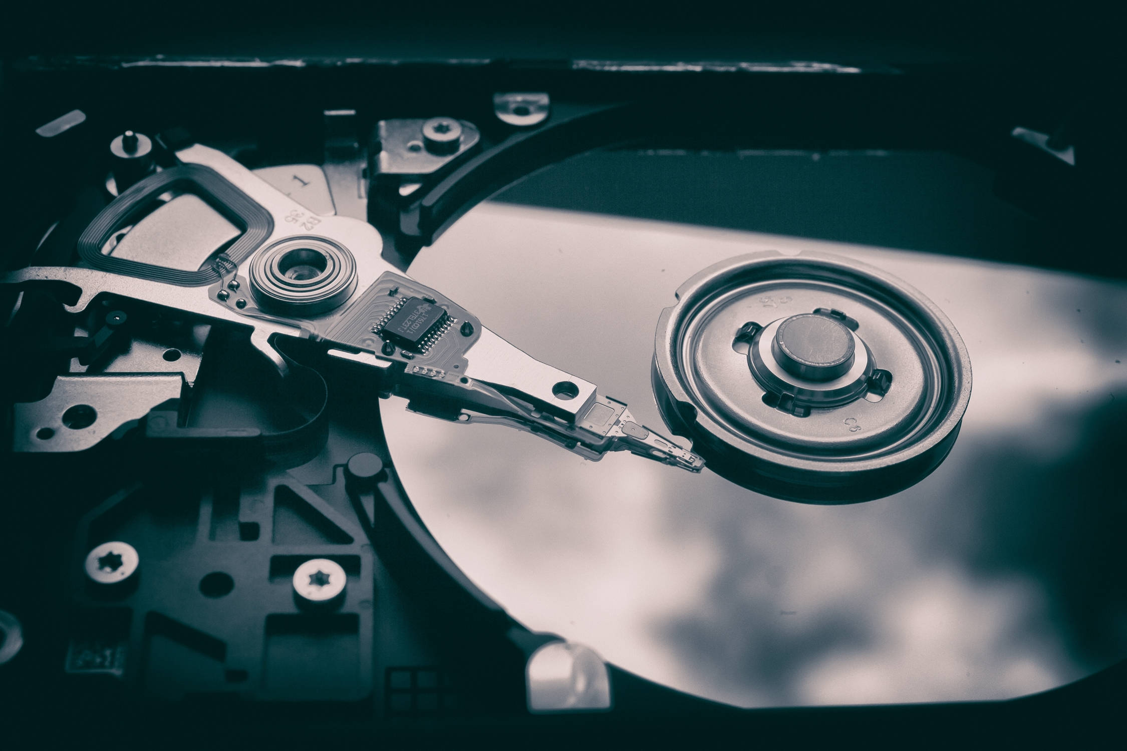 Hard Drive 桌布 壁紙 — 拆解硬碟的特寫，在氣氛深沉的青綠色燈光下顯露出旋轉碟片和讀寫頭。