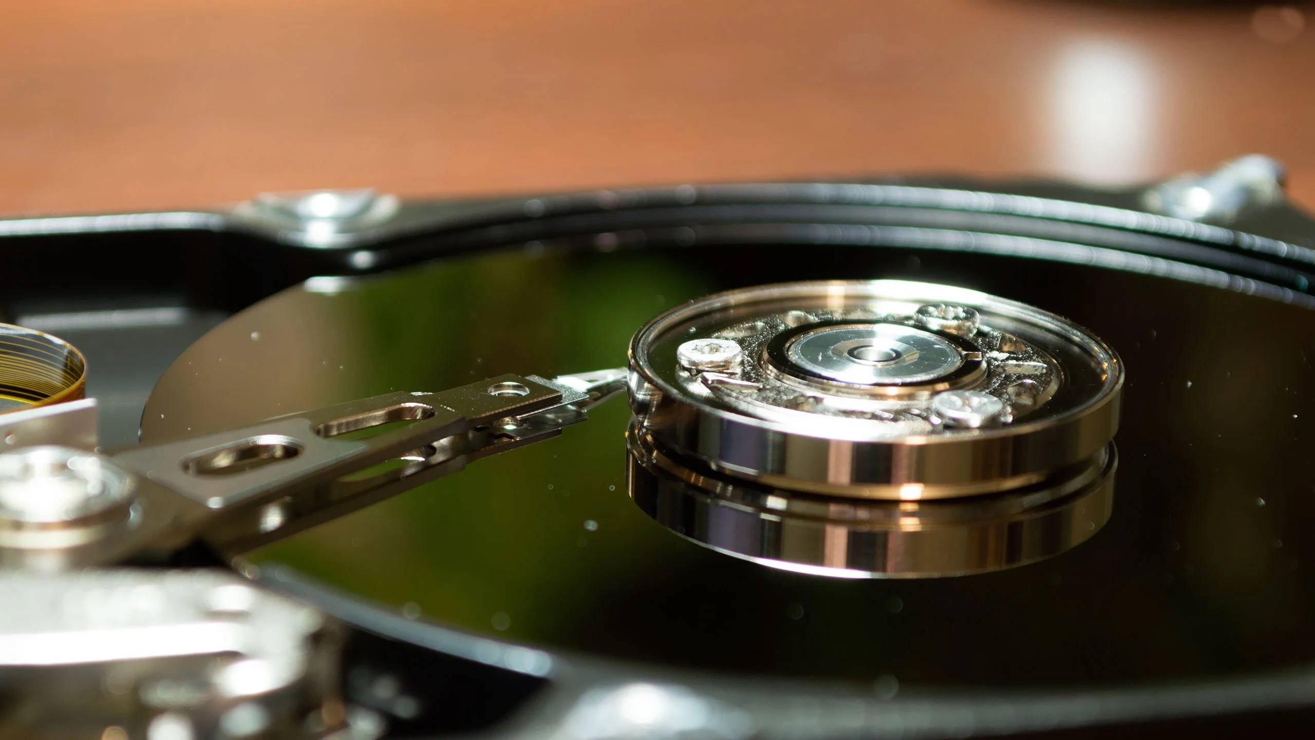 Hard Drive 桌布 壁紙 — 拆解硬碟的特寫，露出閃亮的金屬碟片和讀寫臂，背景為模糊的木質表面。