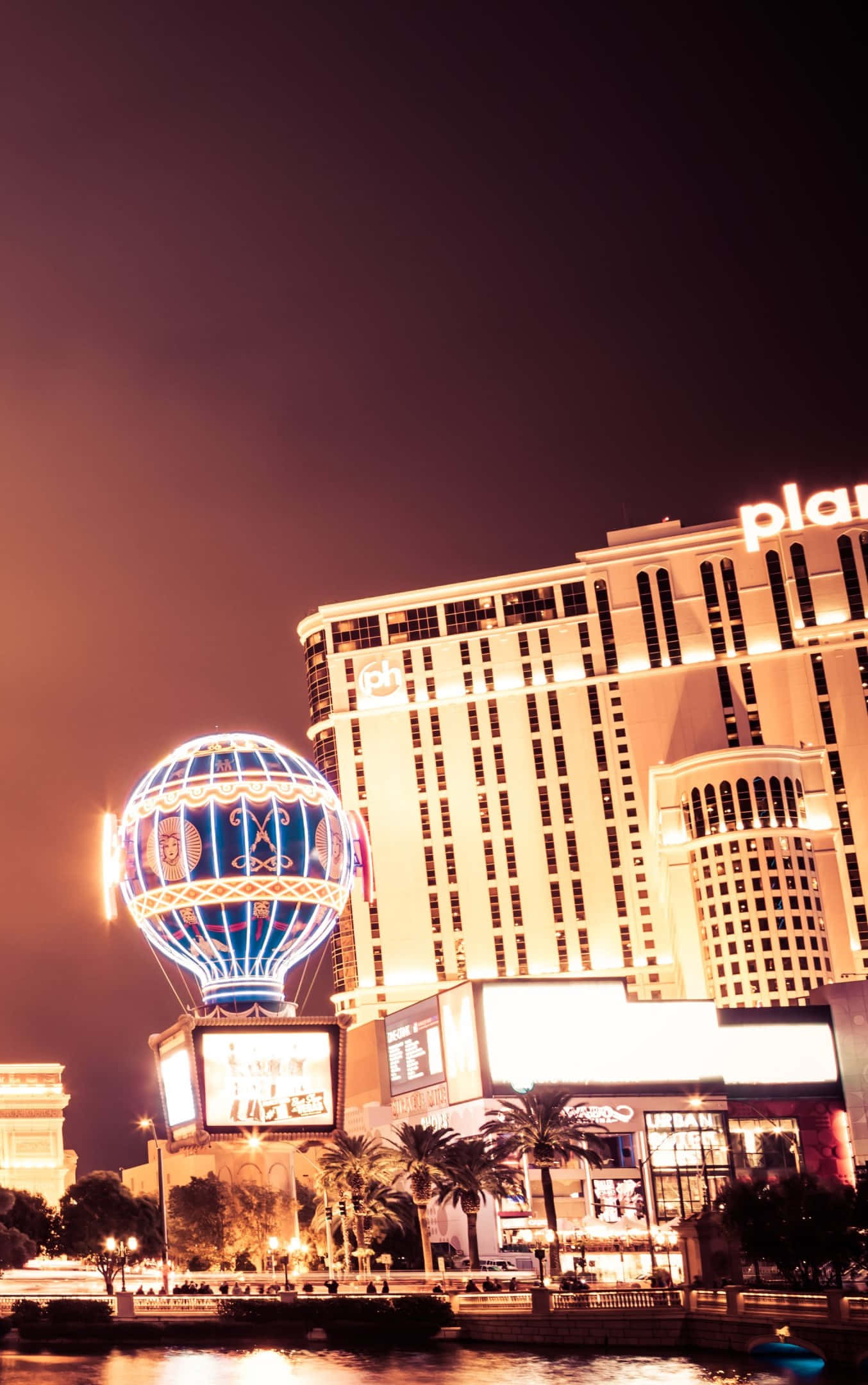 拉斯維加斯之夜 桌布 壁紙 — 拉斯維加斯 Planet Hollywood Resort 的迷人夜景，沿水道有發光的熱氣球雕塑和棕櫚樹。