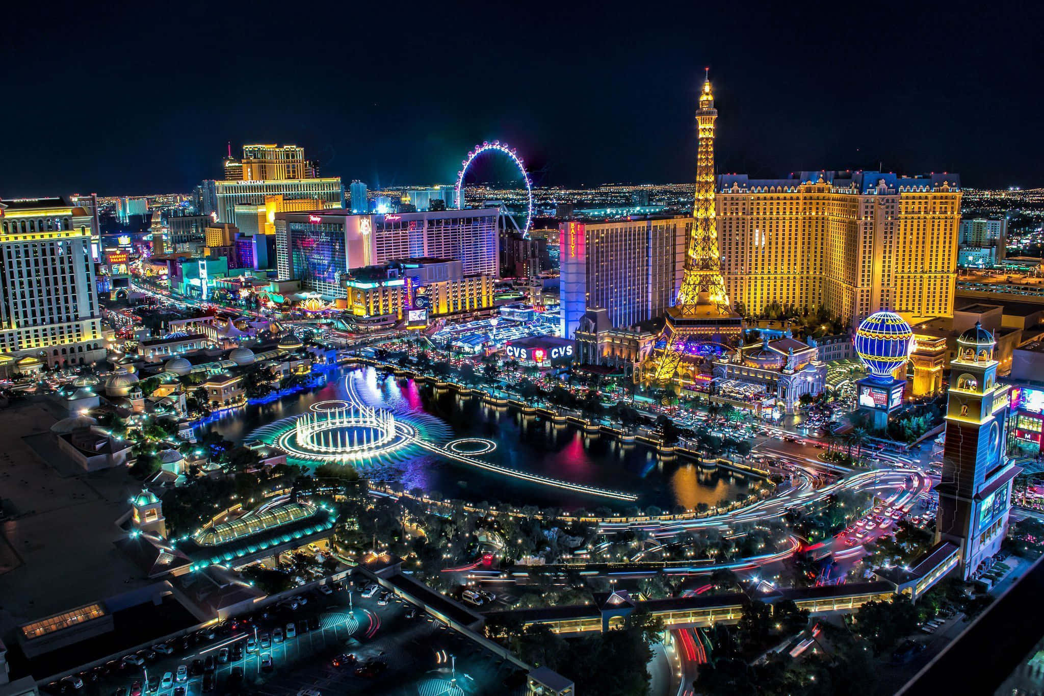 Las Vegas 桌布 壁紙 — 拉斯維加斯令人目眩的夜景，展現了燈火通明的酒店、艾菲爾鐵塔複製品，以及在水面上反射的鮮豔霓虹燈。