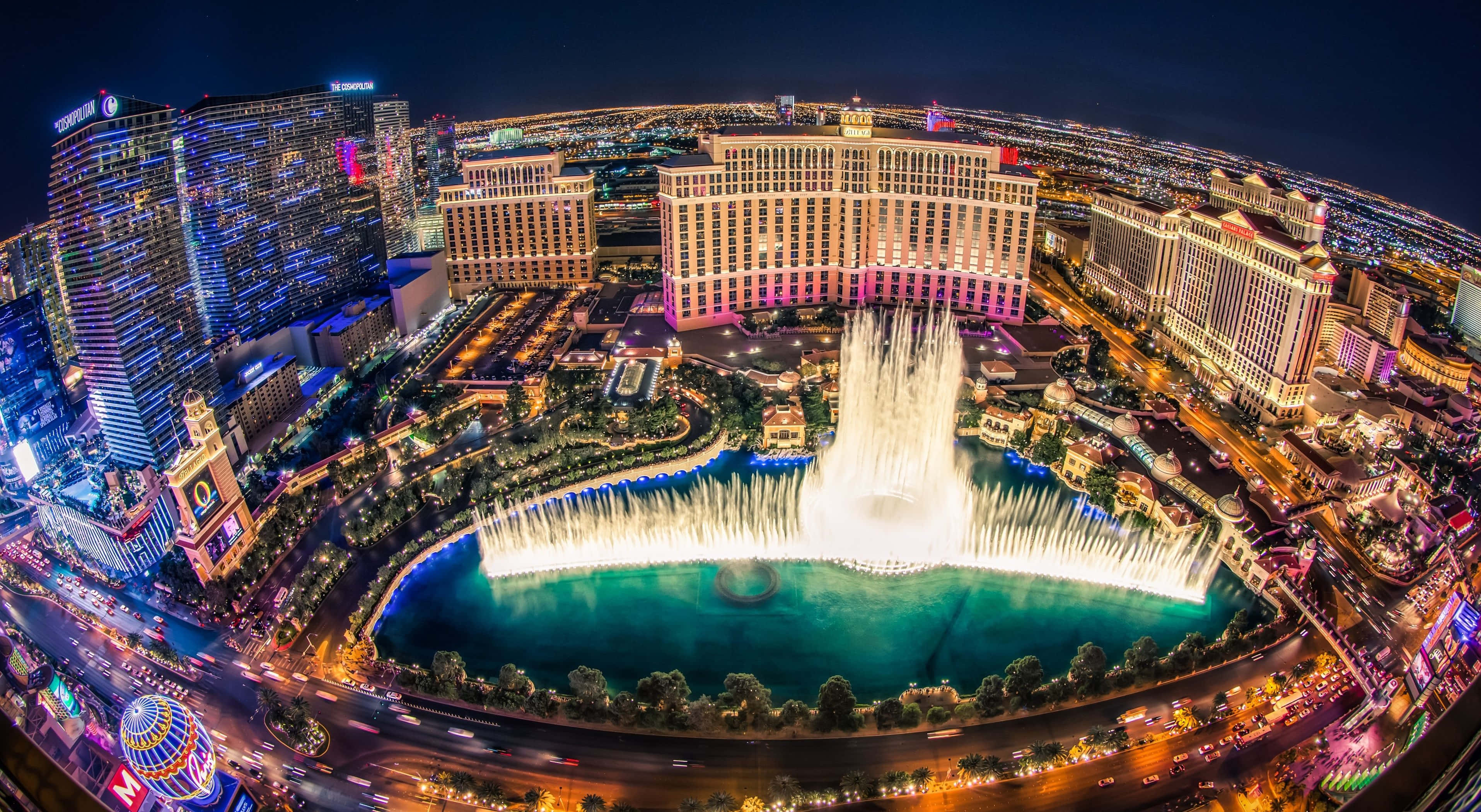 4K Las Vegas 桌布 壁紙 — 拉斯維加斯令人眼花撩亂的夜間空中景觀，展示了標誌性的貝拉吉奧噴泉與耀眼燈光和摩天大樓同步舞動。