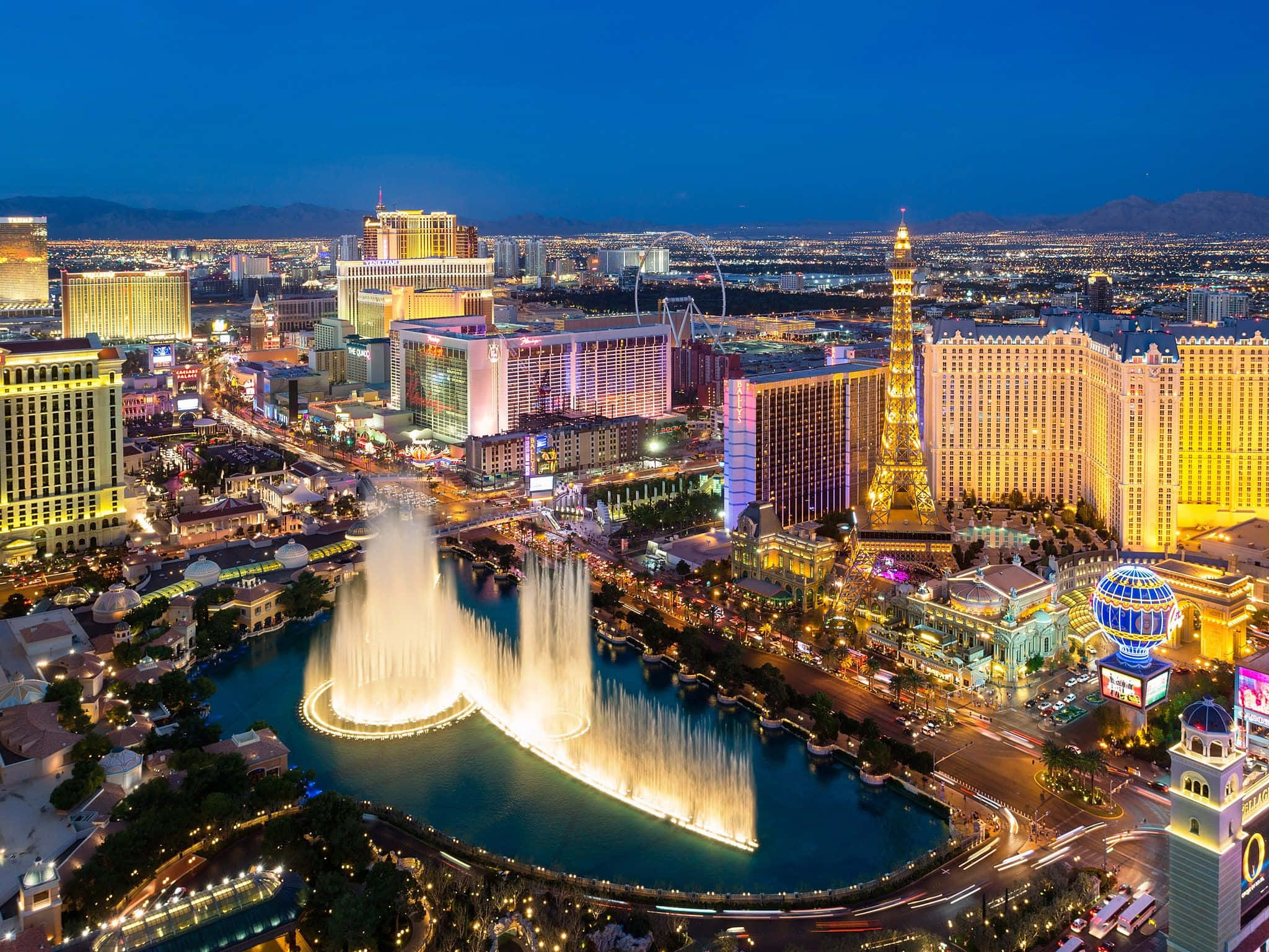 Las Vegas Skyline 桌布 壁紙 — 拉斯維加斯令人眼花撩亂的夜間空中景觀，在深藍色天空下展示著燈光璀璨的噴泉和標誌性酒店。