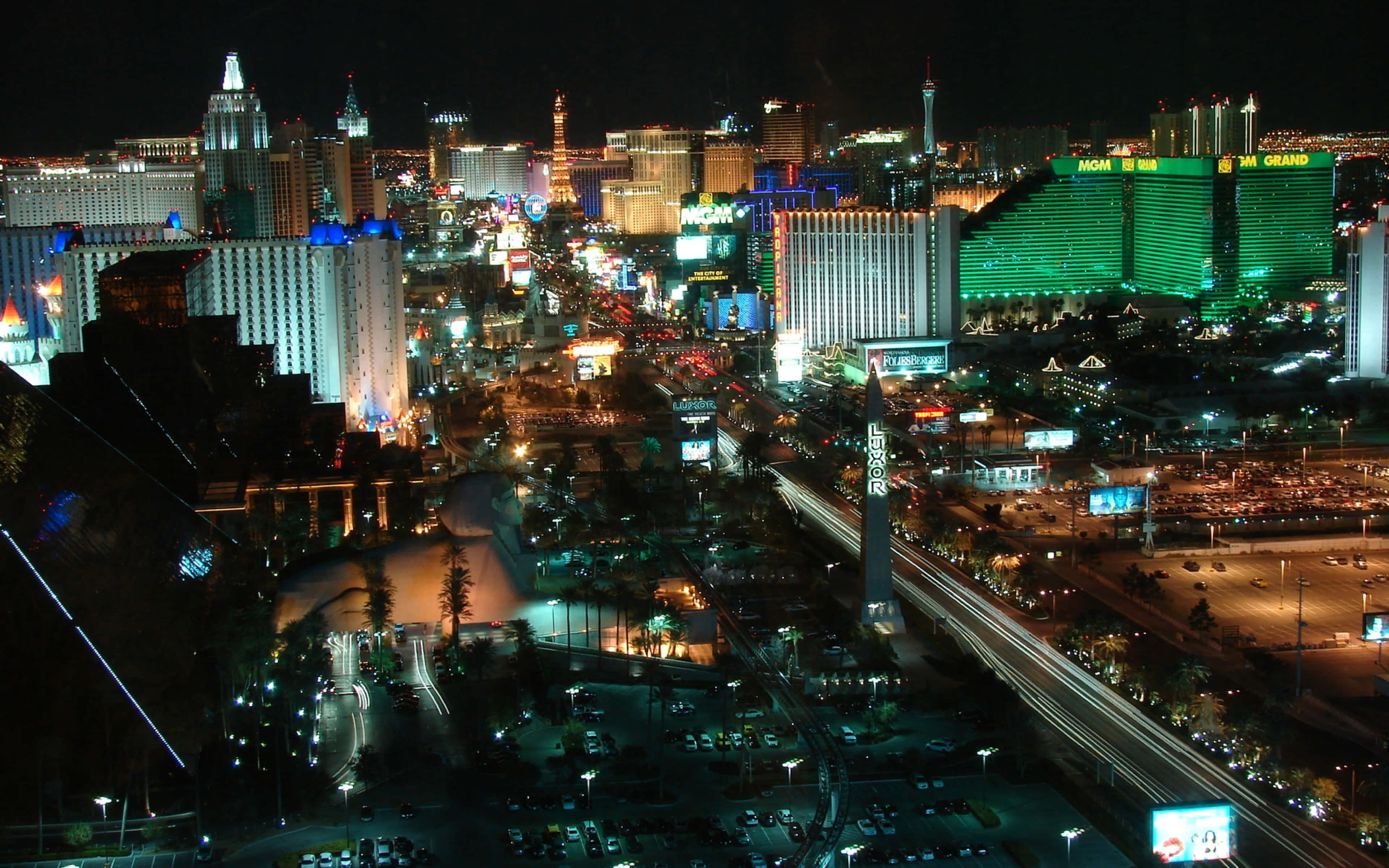 4K Las Vegas 桌布 壁紙 — 拉斯維加斯令人眼花撩亂的夜間空中景觀，展示霓虹燈閃爍的飯店和充滿發光招牌及車流痕跡的繁華街道。