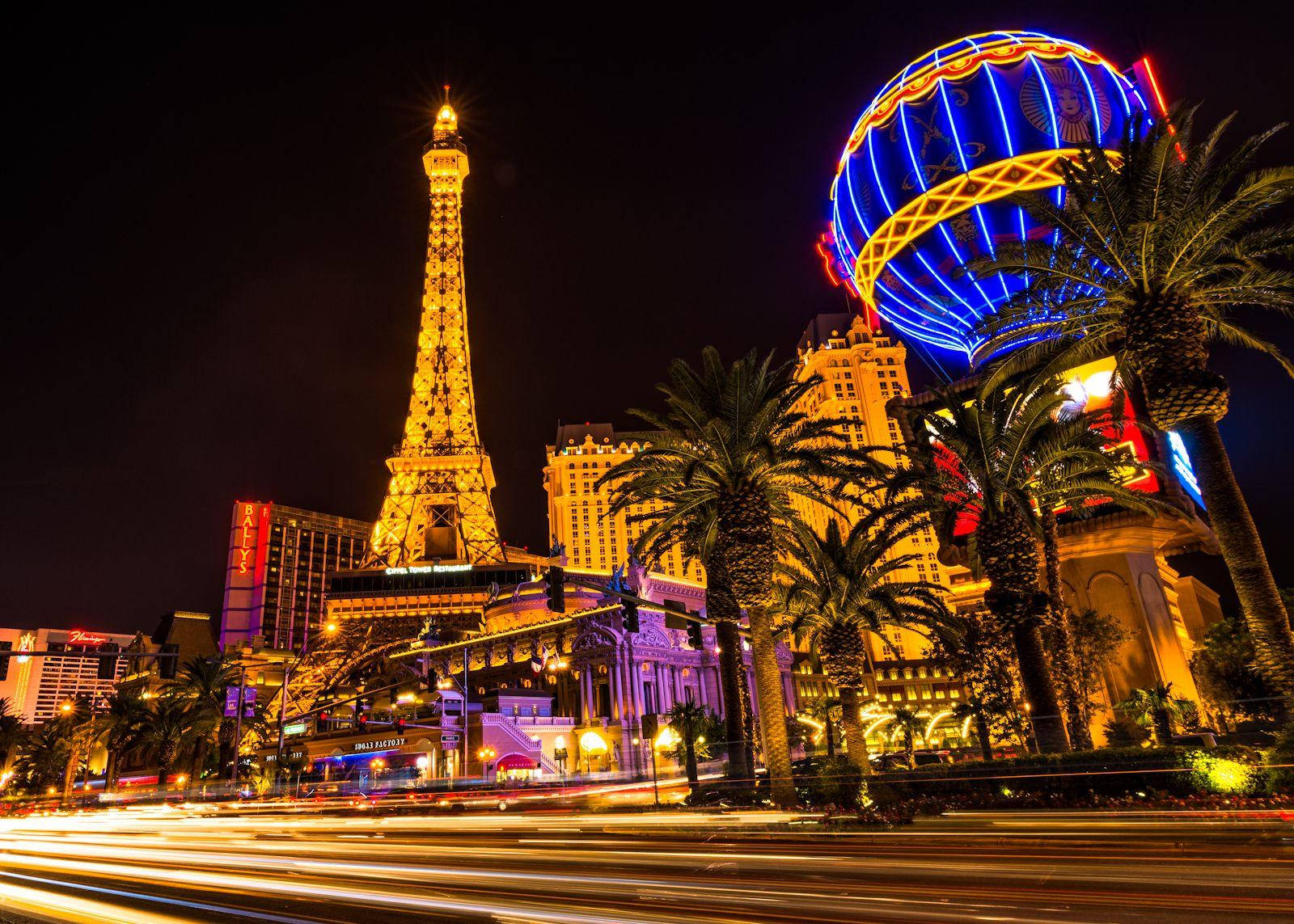 Eiffel Tower 桌布 壁紙 — 拉斯維加斯令人眼花繚亂的夜景，閃耀的艾菲爾鐵塔複製品和巨大的藍色霓虹地球儀，周圍環繞著棕櫚樹和流動的城市燈光。