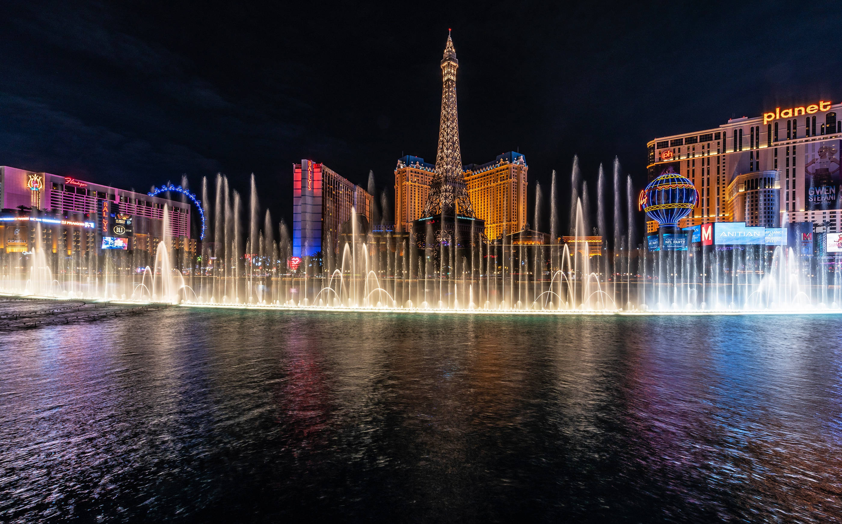 Las Vegas 桌布 壁紙 — 拉斯維加斯令人眼花繚亂的夜間噴泉表演，發光的噴射水流在水面上反射，背後閃耀著艾菲爾鐵塔複製品。