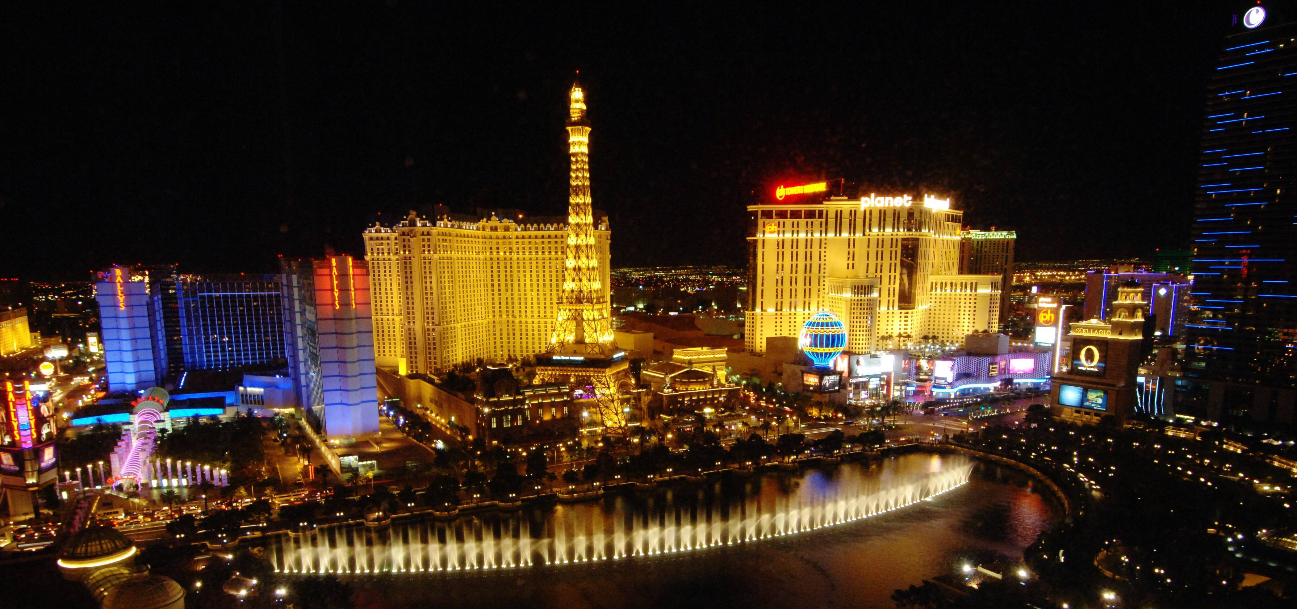 Las Vegas 桌布 壁紙 — 拉斯維加斯令人驚嘆的夜間空中景觀，展示燈火通明的酒店和反映霓虹燈光的活力噴泉表演。