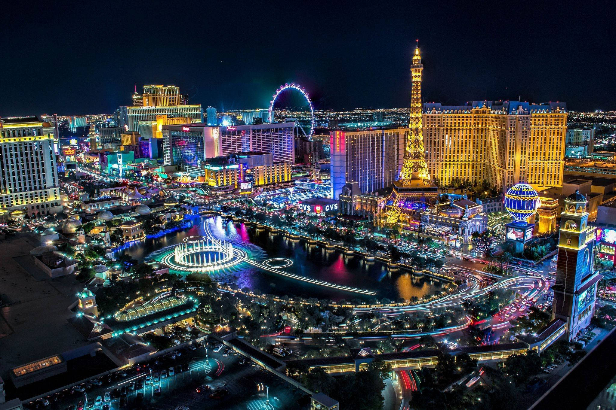Las Vegas 桌布 壁紙 — 拉斯維加斯令人驚嘆的夜間空中景觀，展示了艾菲爾鐵塔複製品和在水面上反射的鮮豔霓虹燈。