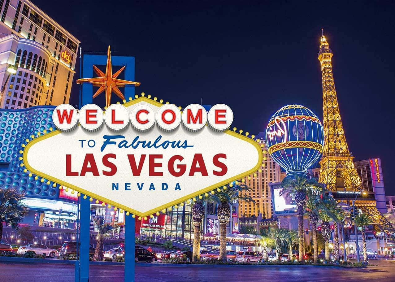 Nevada 桌布 壁紙 — 拉斯維加斯充滿活力的夜景，標誌性的歡迎標誌在霓虹燈下閃耀，背景是艾菲爾鐵塔複製品和熱氣球。