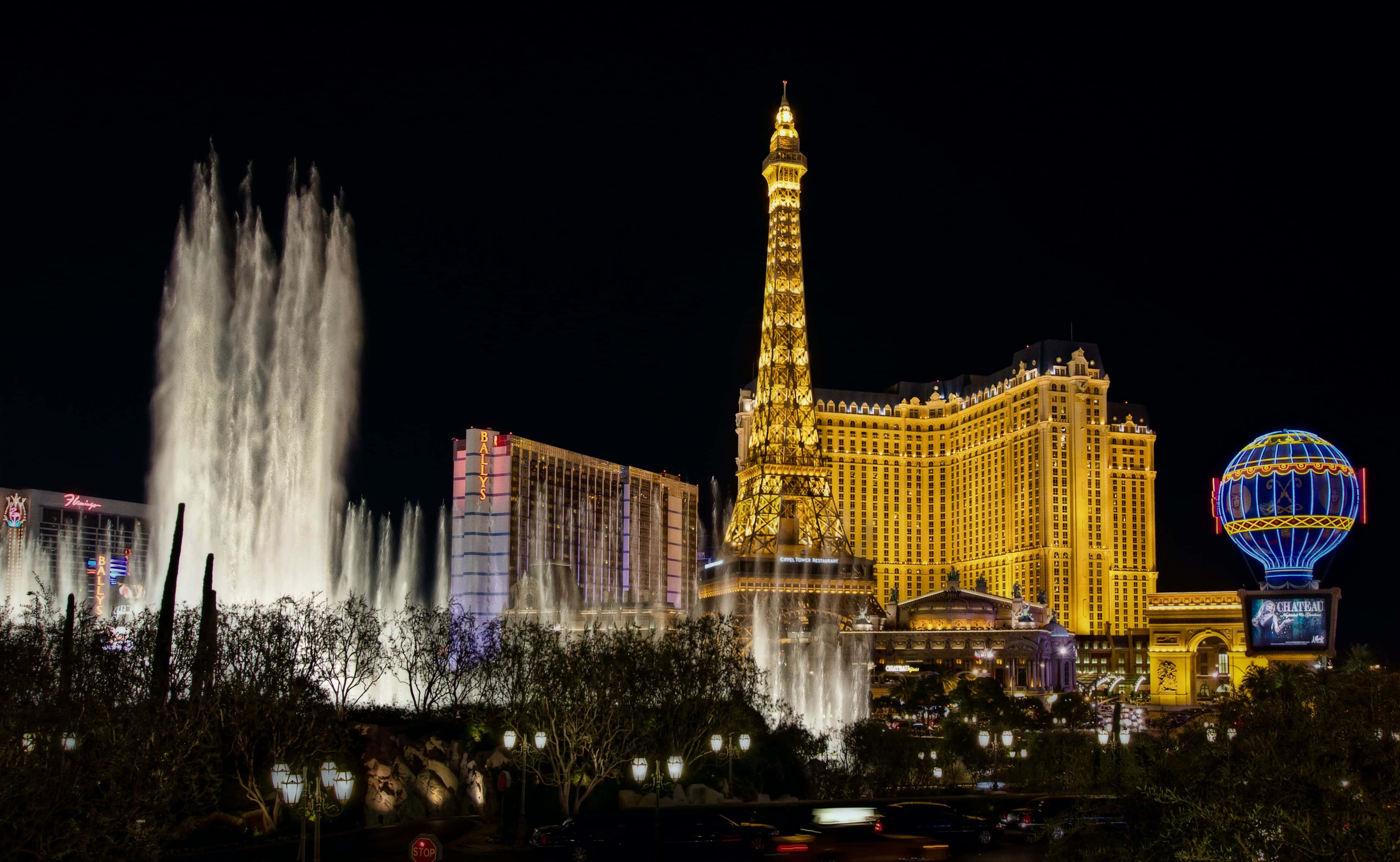 4K Las Vegas 桌布 壁紙 — 拉斯維加斯大道上令人眼花撩亂的夜景，包括發光的艾菲爾鐵塔複製品和巨大的噴泉表演。