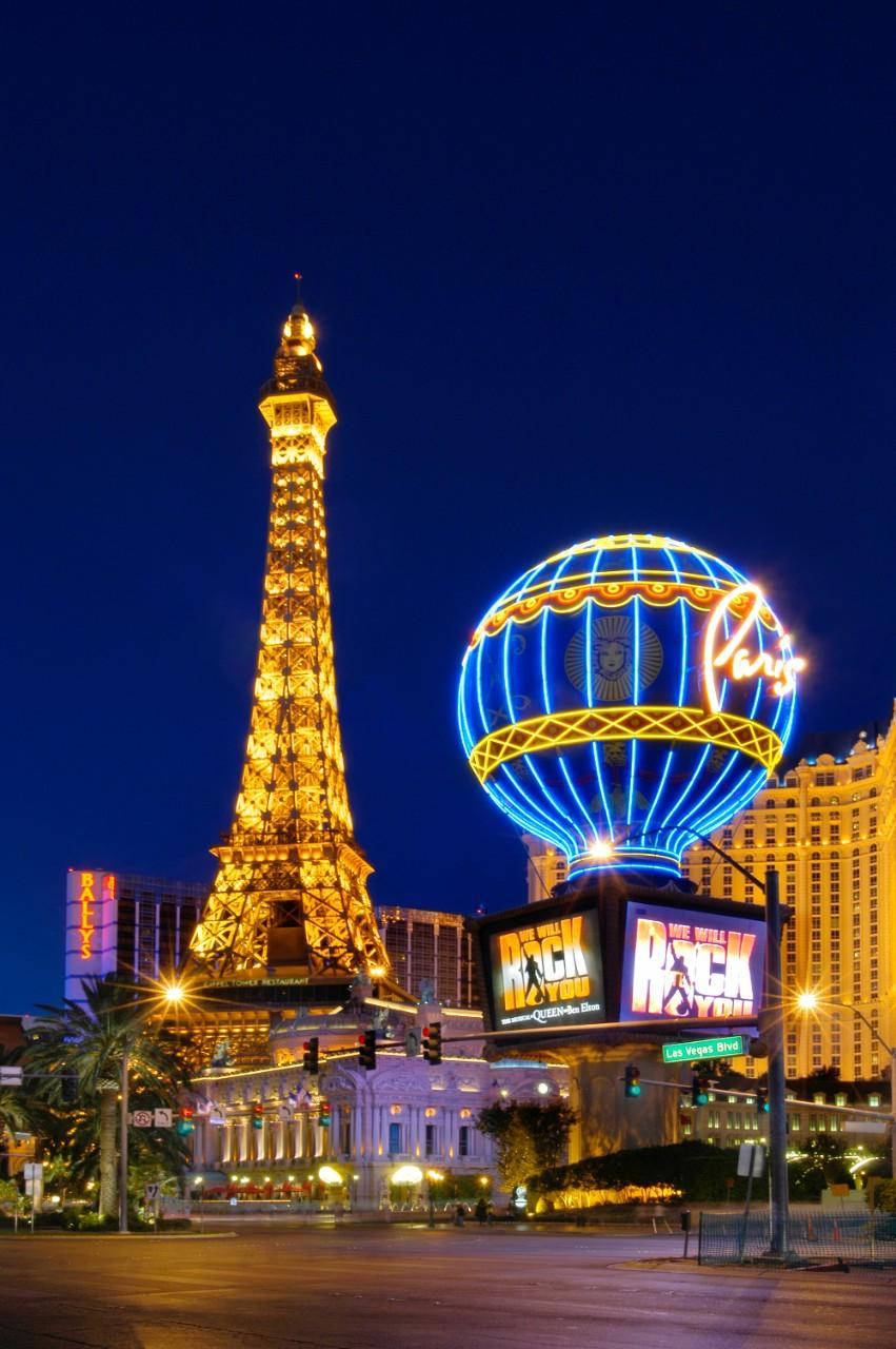 Vegas iPhone 桌布 壁紙 — 拉斯維加斯大道上璀璨的夜景，以發光的艾菲爾鐵塔複製品和充滿活力的藍色熱氣球標誌為特色。