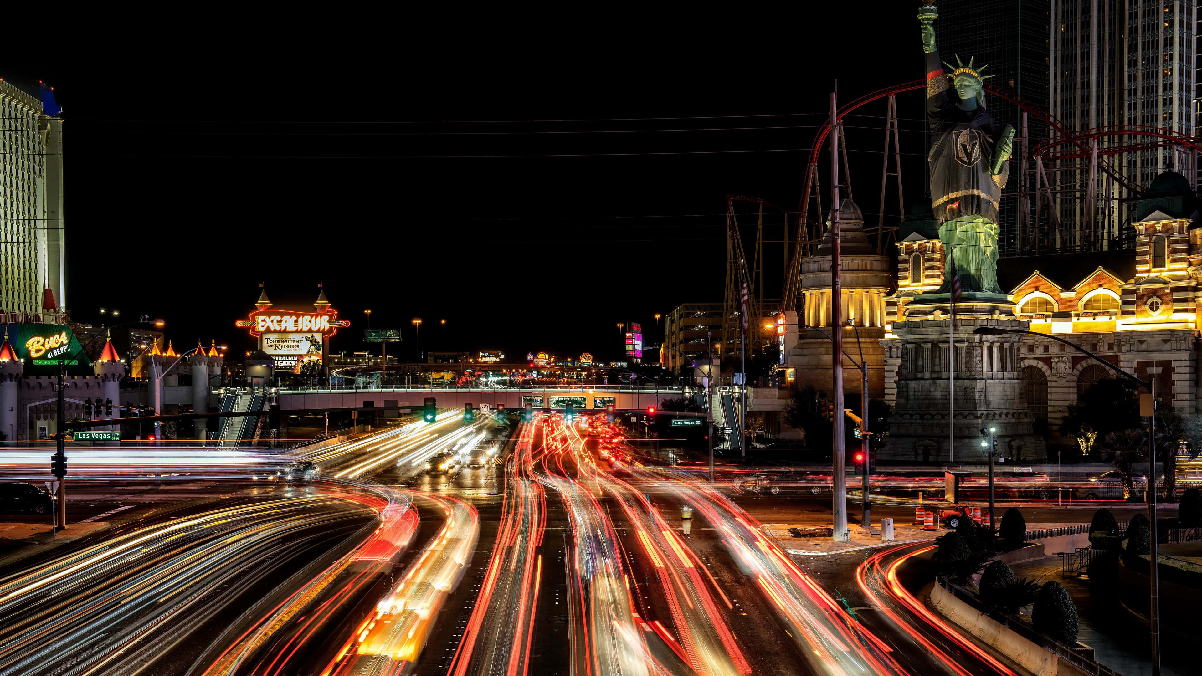 4K Las Vegas 桌布 壁紙 — 拉斯維加斯大道上車流形成的充滿活力的夜間光軌，標誌性的自由女神像複製品和閃爍的賭場招牌。