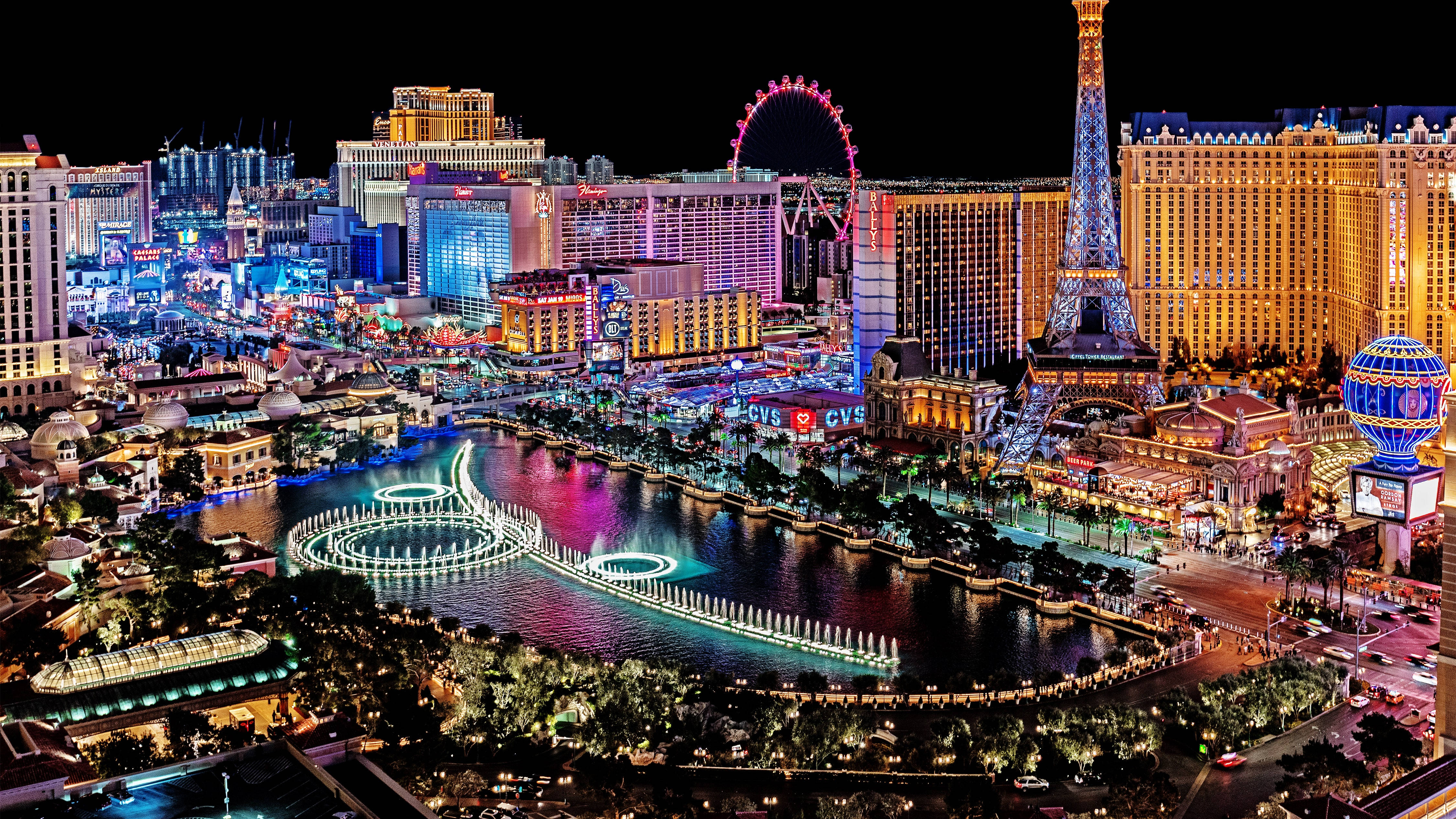 Las Vegas 4K 桌布 壁紙 — 拉斯維加斯大道充滿活力的夜景，耀眼的霓虹燈光倒映在噴泉和艾菲爾鐵塔等標誌性複製品上。