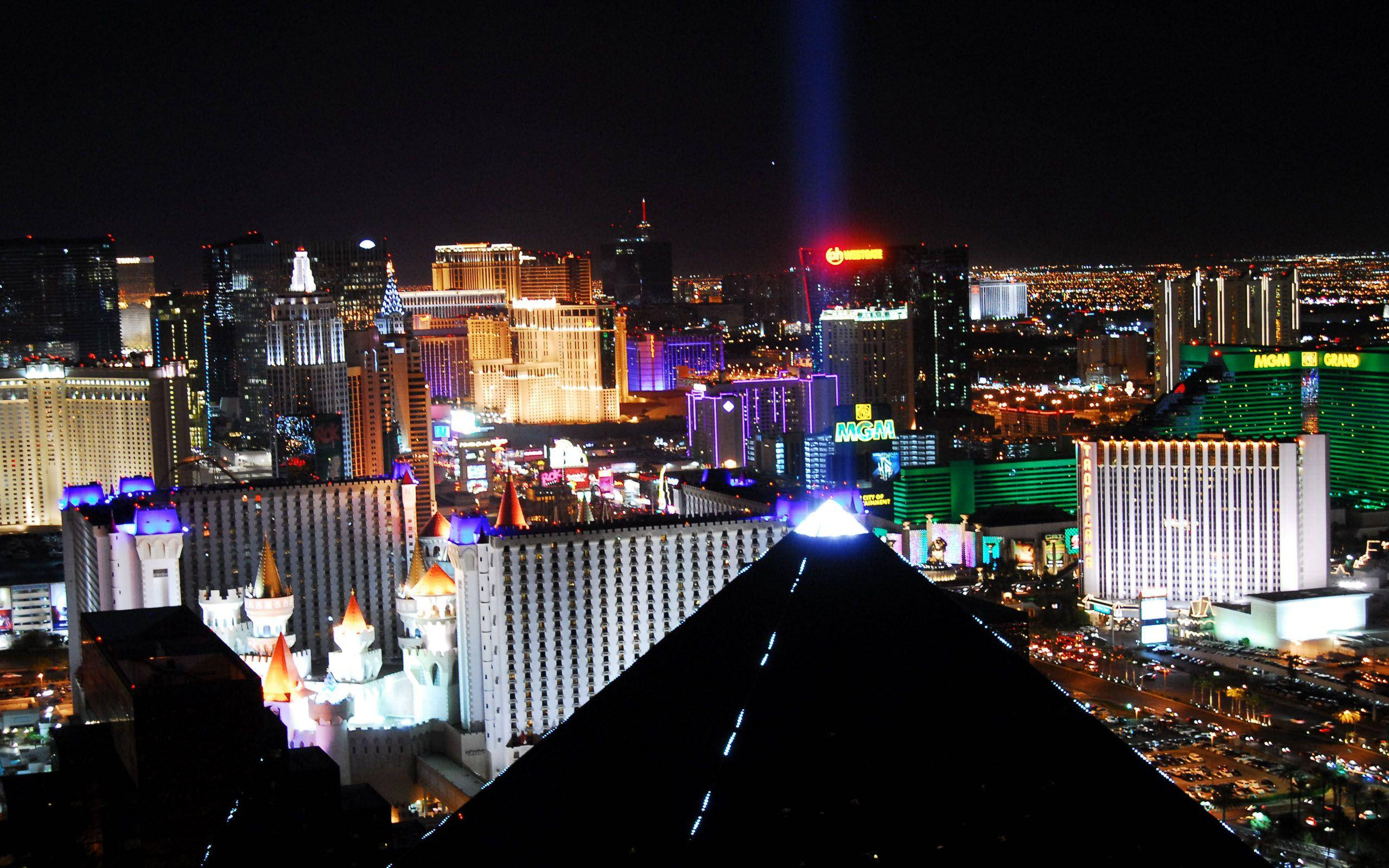 拉斯維加斯 桌布 壁紙 — 拉斯維加斯天際線的迷人夜景，霓虹燈閃爍的酒店和一道高聳的光束劃破黑暗的天空。
