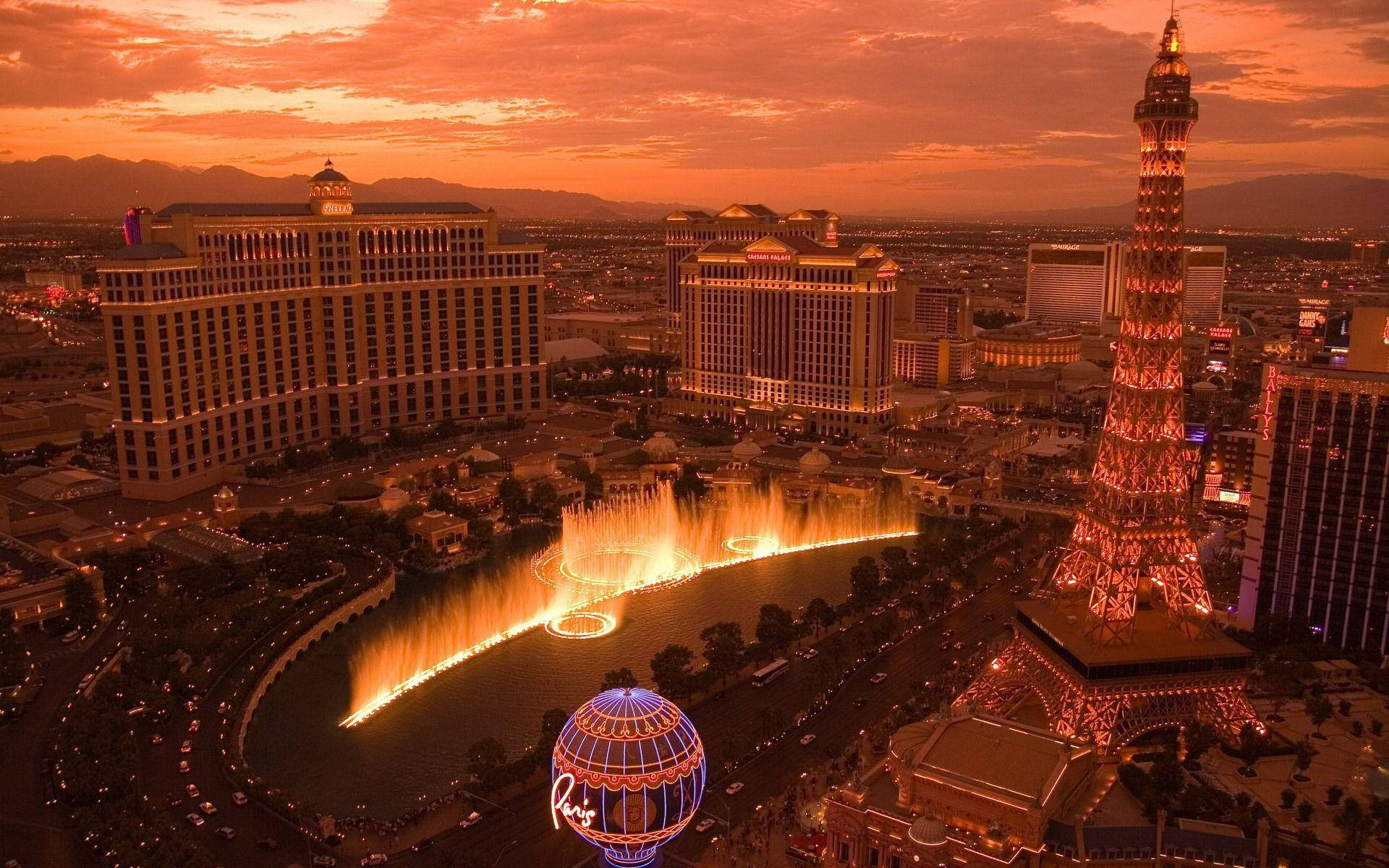Las Vegas 桌布 壁紙 — 拉斯維加斯日落時分的鳥瞰圖，噴泉燈光璀璨，複製的艾菲爾鐵塔在橙色天空下閃耀。
