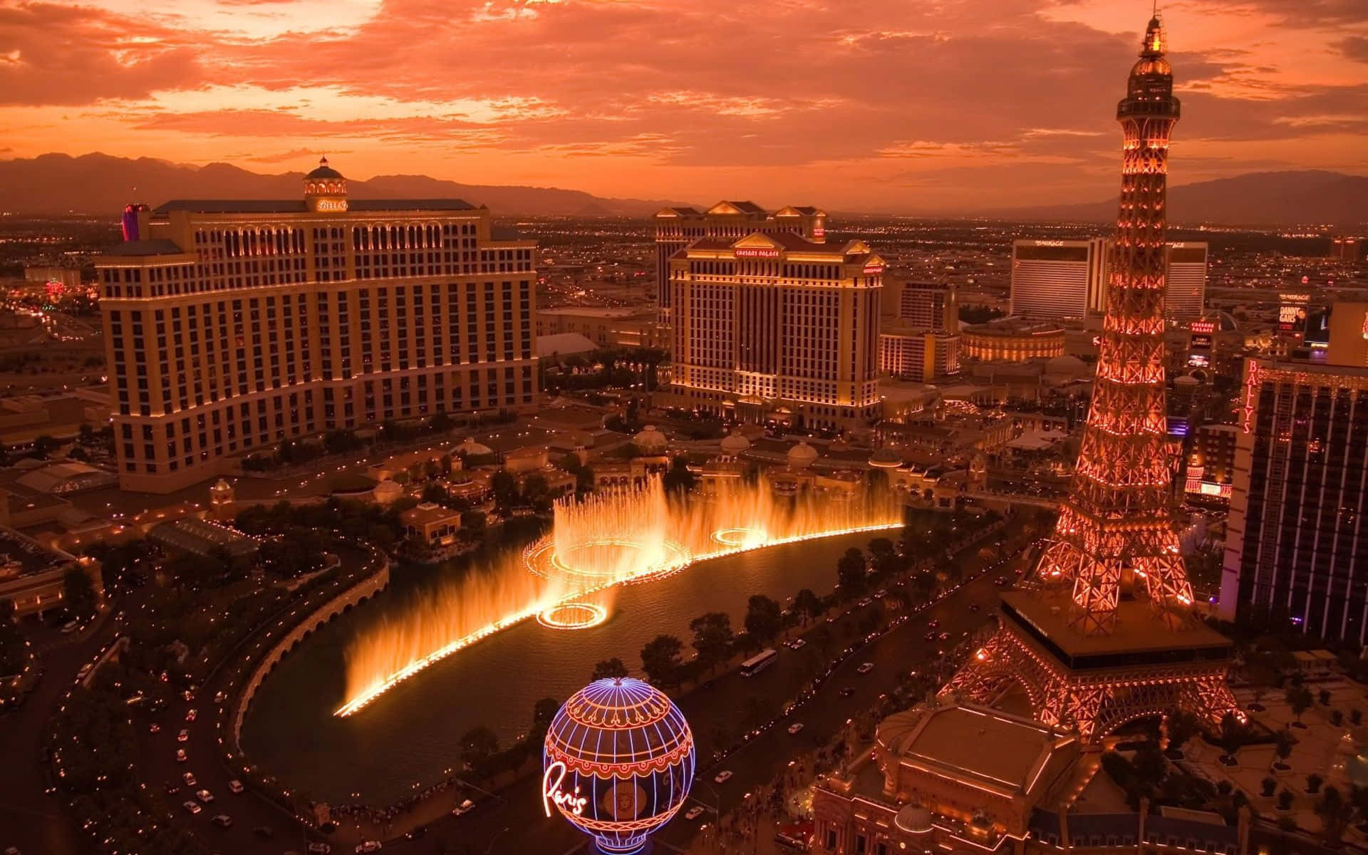 Las Vegas Skyline 桌布 壁紙 — 拉斯維加斯日落時分的鳥瞰圖，燈光璀璨的噴泉和複製的艾菲爾鐵塔在橙色天空下閃耀。
