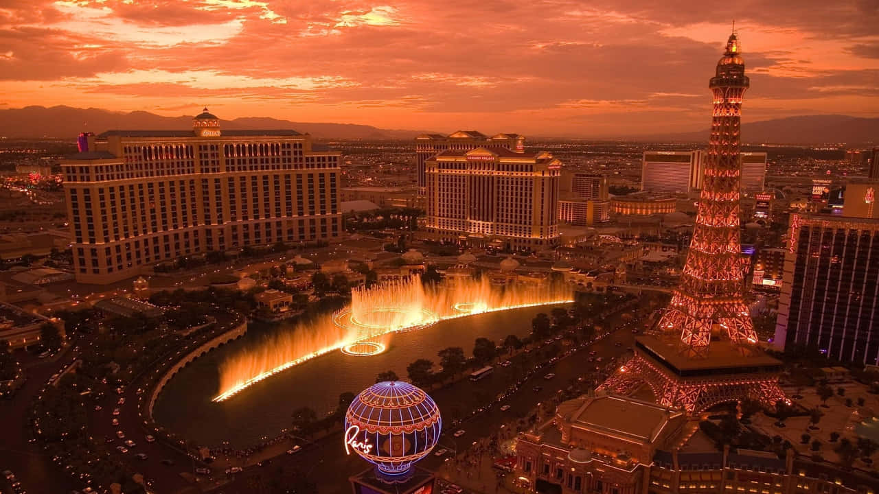 720p Las Vegas 桌布 壁紙 — 拉斯維加斯日落時分的鳥瞰圖，燈光璀璨的噴泉和複製的艾菲爾鐵塔在橙色天空下閃耀。