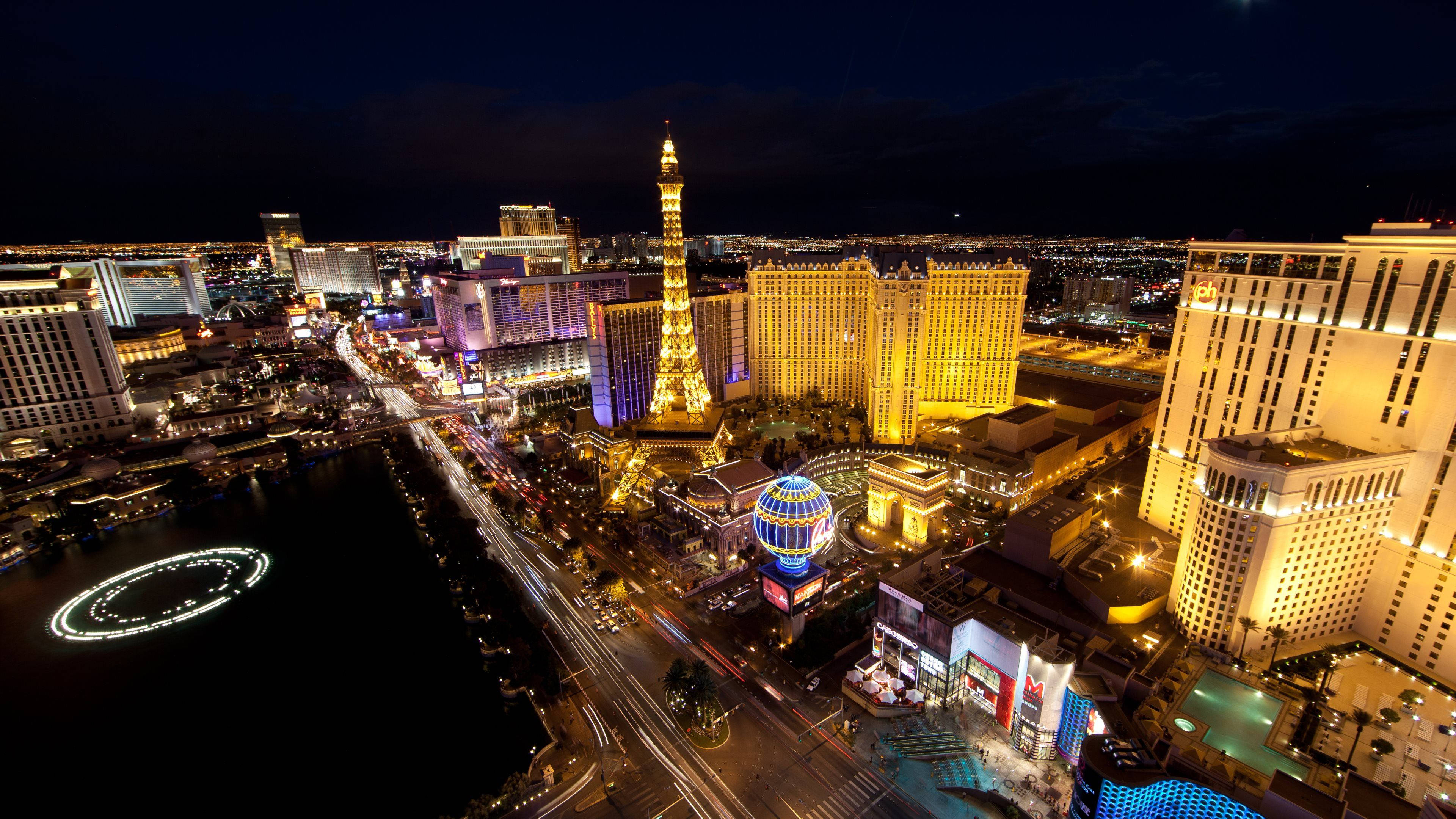 Las Vegas 桌布 壁紙 — 拉斯維加斯的夜間空中景觀，展示燈火通明的酒店和艾菲爾鐵塔複製品，街道和水中景觀閃爍發光。