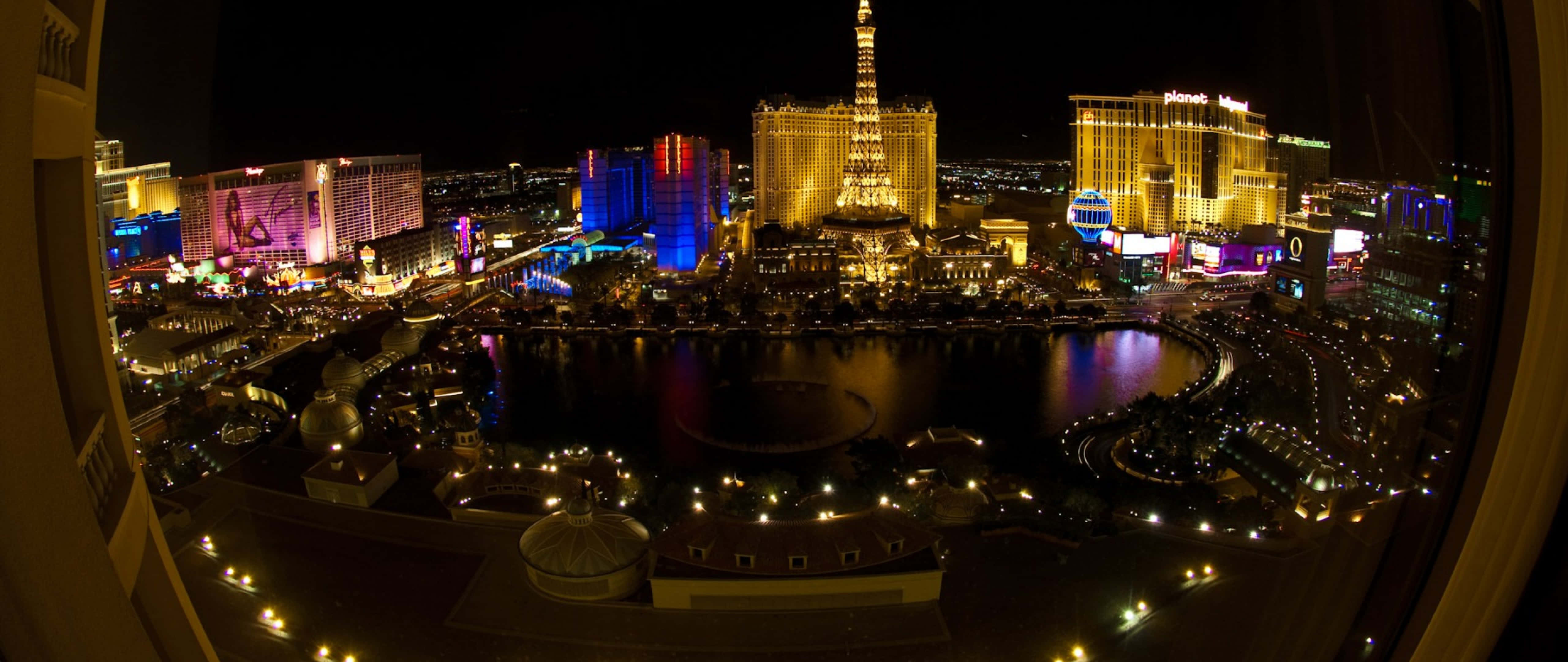 4K Las Vegas 桌布 壁紙 — 拉斯維加斯的魚眼夜景，展現耀眼的霓虹燈光和標誌性酒店在黑暗水道上的倒影。