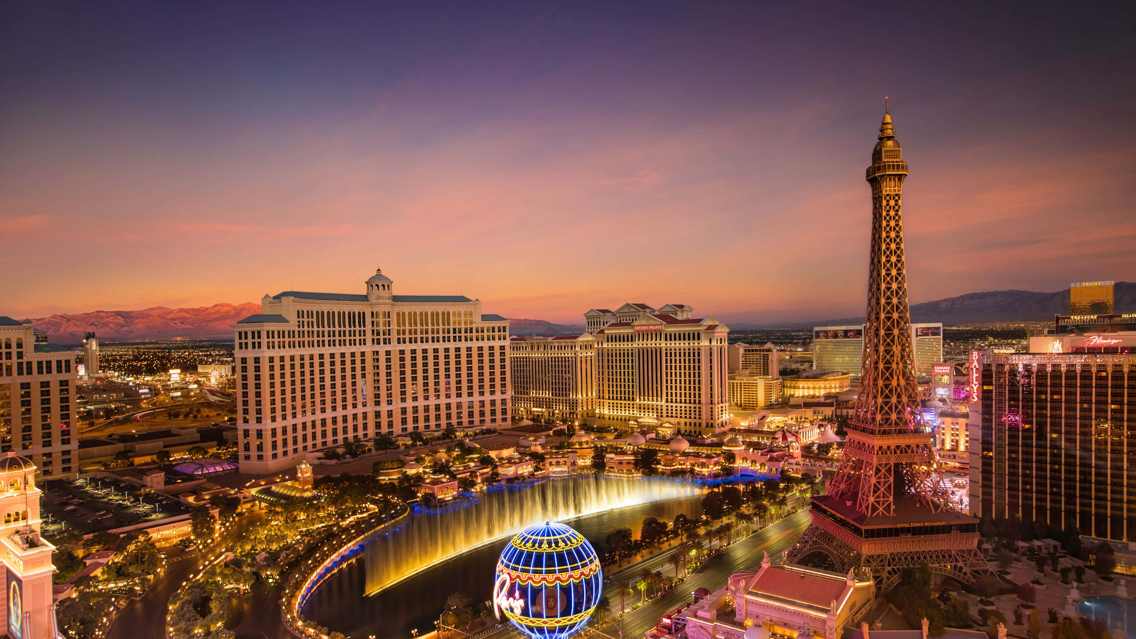 Las Vegas 桌布 壁紙 — 拉斯維加斯黃昏天際線，燈火通明的酒店、噴泉和複製艾菲爾鐵塔在紫橙色天空中閃耀。