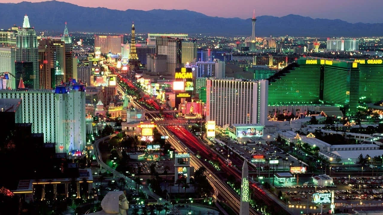 720p Las Vegas 桌布 壁紙 — 拉斯維加斯黃昏時的鳥瞰圖，霓虹燈閃爍的酒店和車流在紫色天空下劃出光軌。